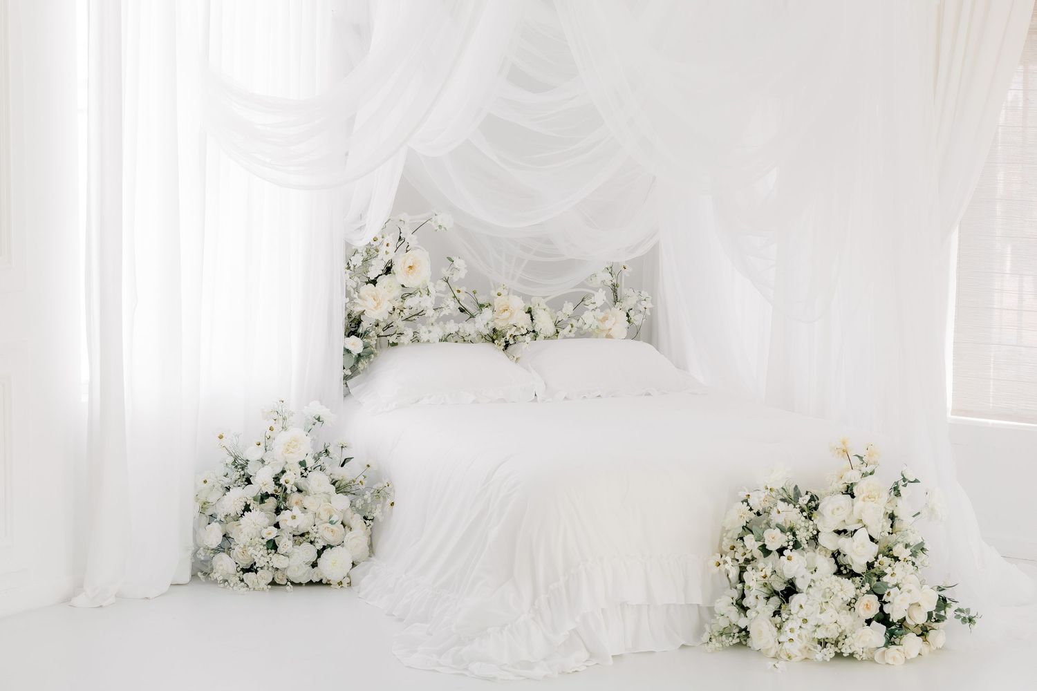 Elegant white wedding backdrop with floral arrangements featuring white roses and draped fabric against a bright background.
