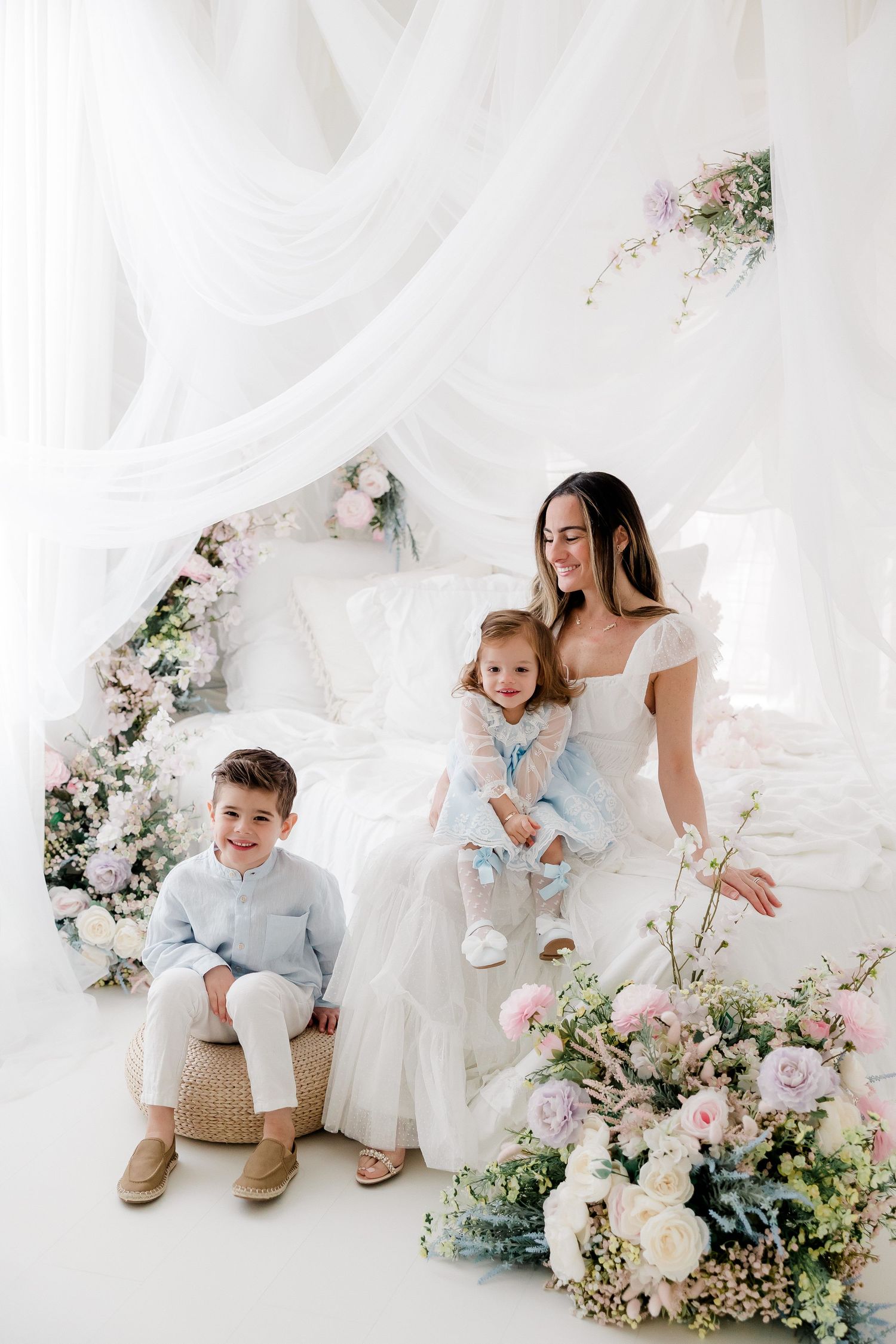 A dreamy family portrait in white with floral decorations featuring soft pink and white roses in an ethereal setting.