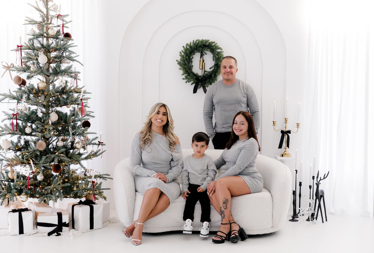 Modern Christmas family photoshoot with grey outfits and decorated tree in white studio.