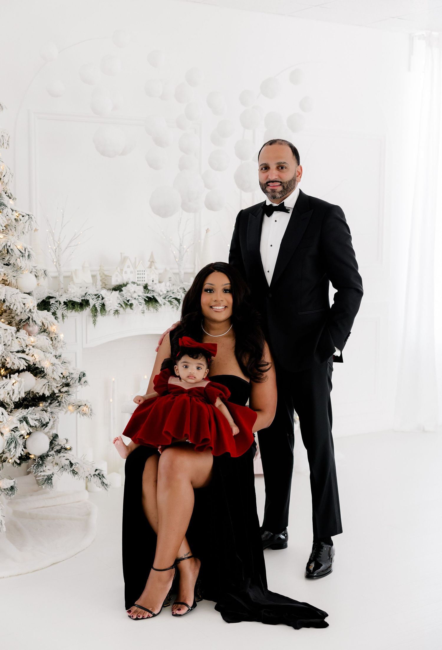 Formal family holiday portraits in black and red attire against a white Christmas backdrop.