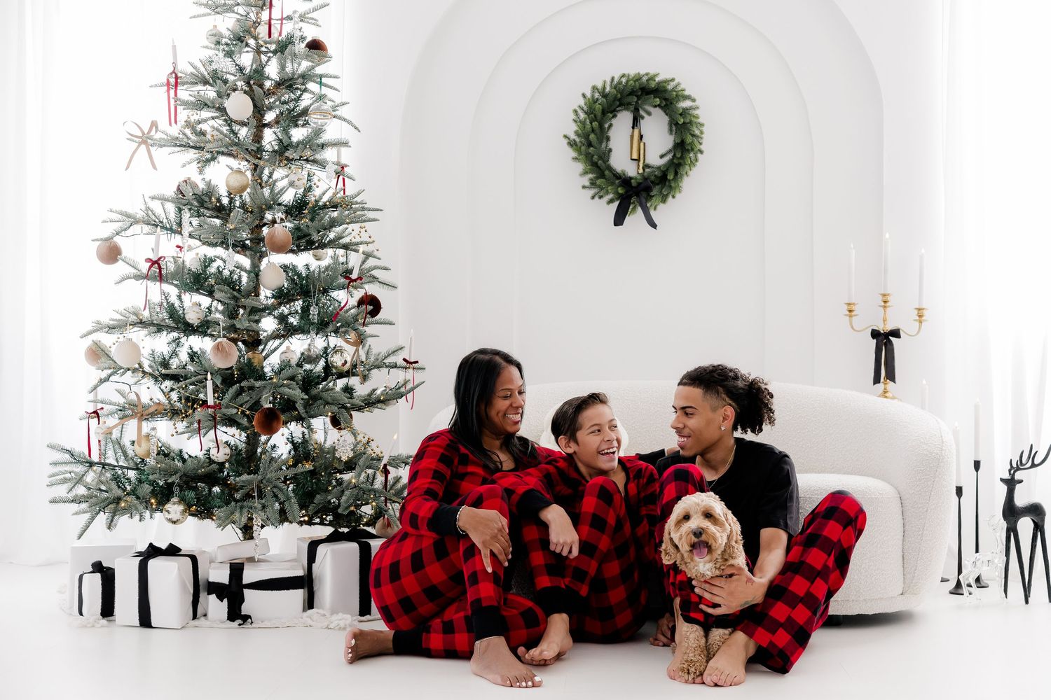 Family in buffalo plaid pajamas lounges by Christmas tree in white studio.