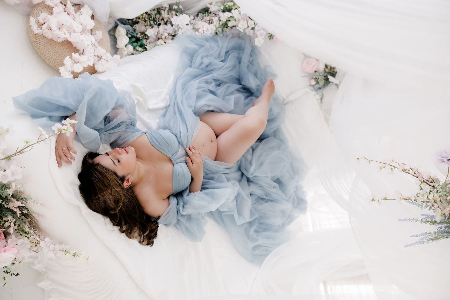 A dreamy boudoir scene with soft blue tulle fabric and delicate cherry blossoms arranged on white bedding.