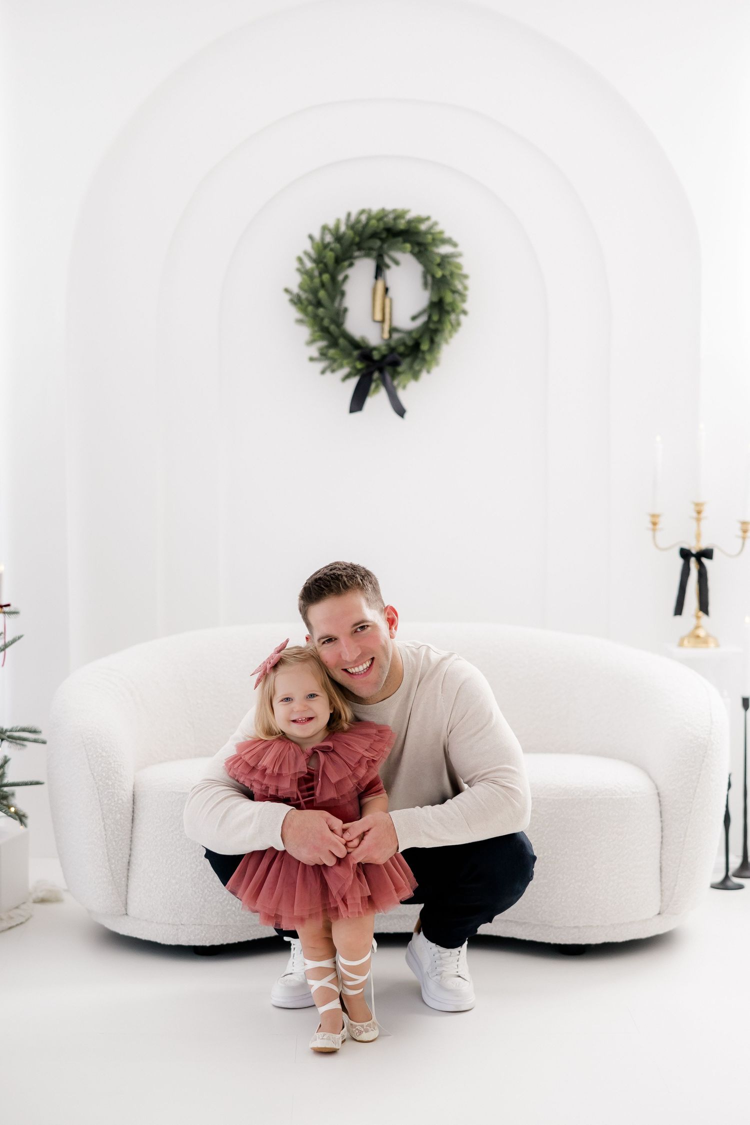 Clean white studio setting with curved walls, wreaths and holiday decor elements.