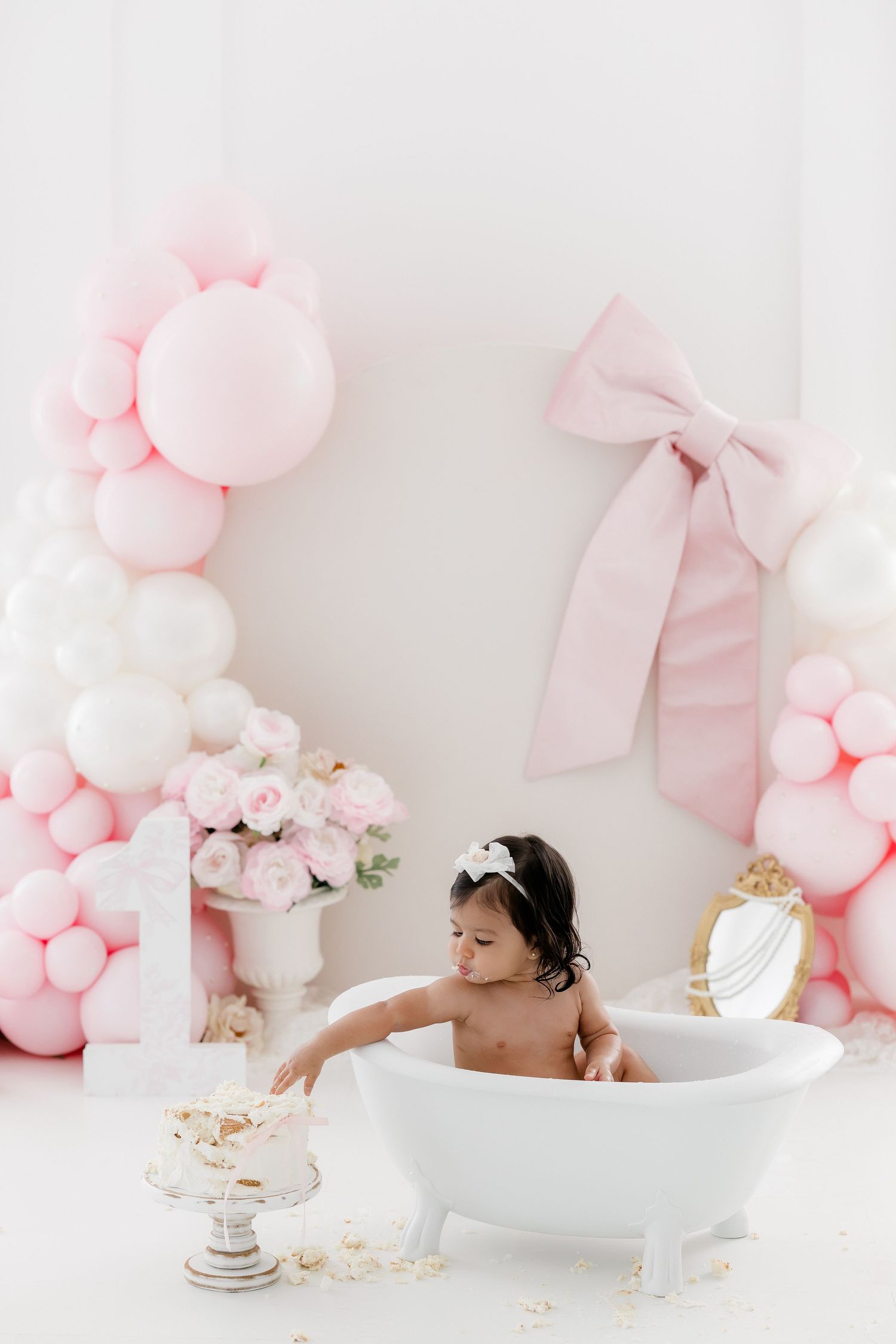 Milk bath photography setup with pink balloons and bows creating a dreamy pastel backdrop for an elegant portrait session.