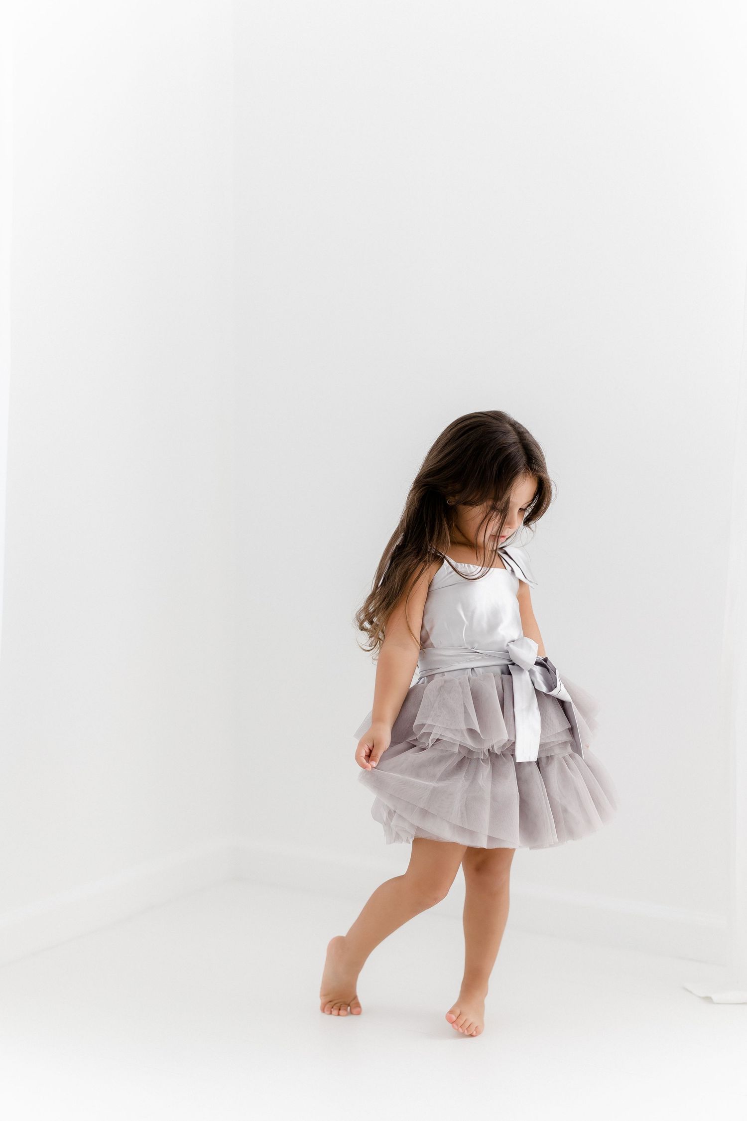 A young dancer in a flowing gray dress twirls gracefully across a white studio floor in a series of dynamic poses.