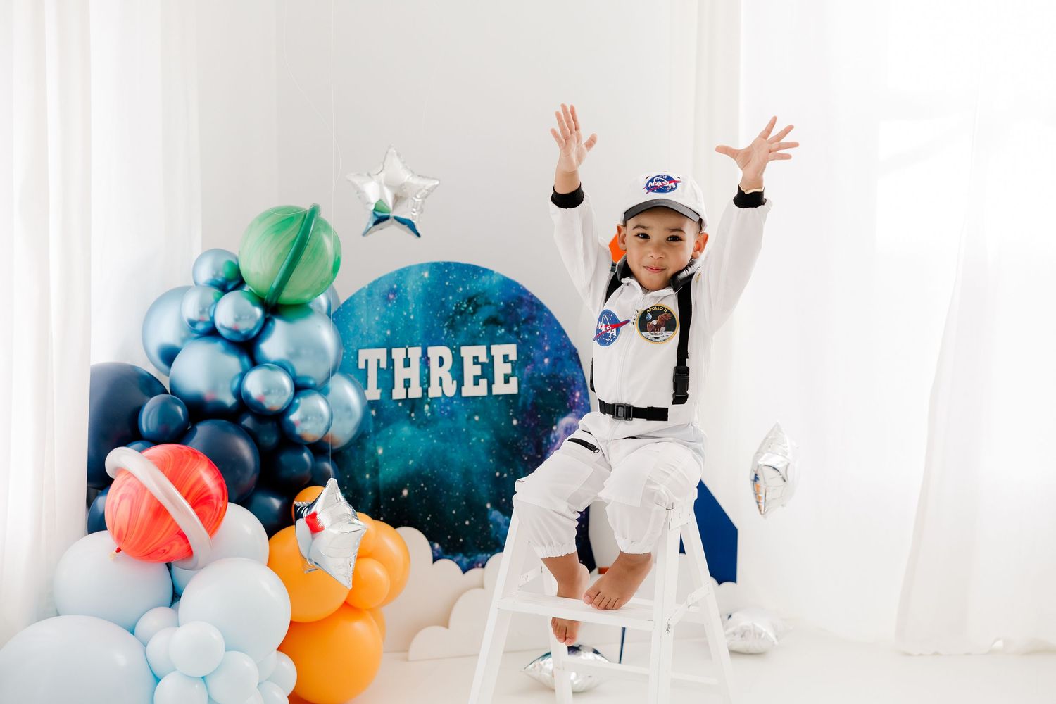 Children in protective white suits and masks play with colorful balloons in a bright indoor space.