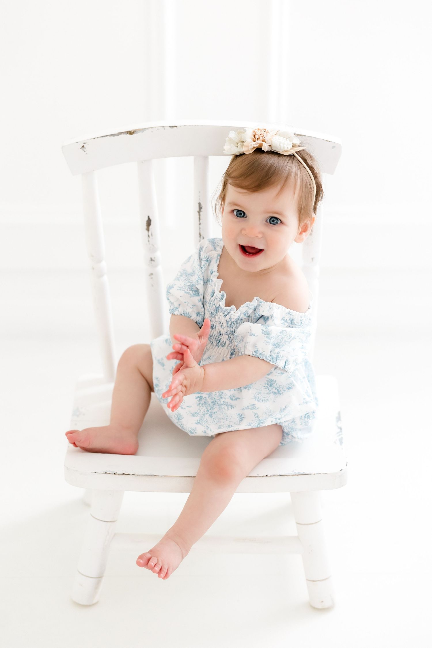 Sweet baby in light blue floral dress crawls and plays on white floor in bright studio setting.