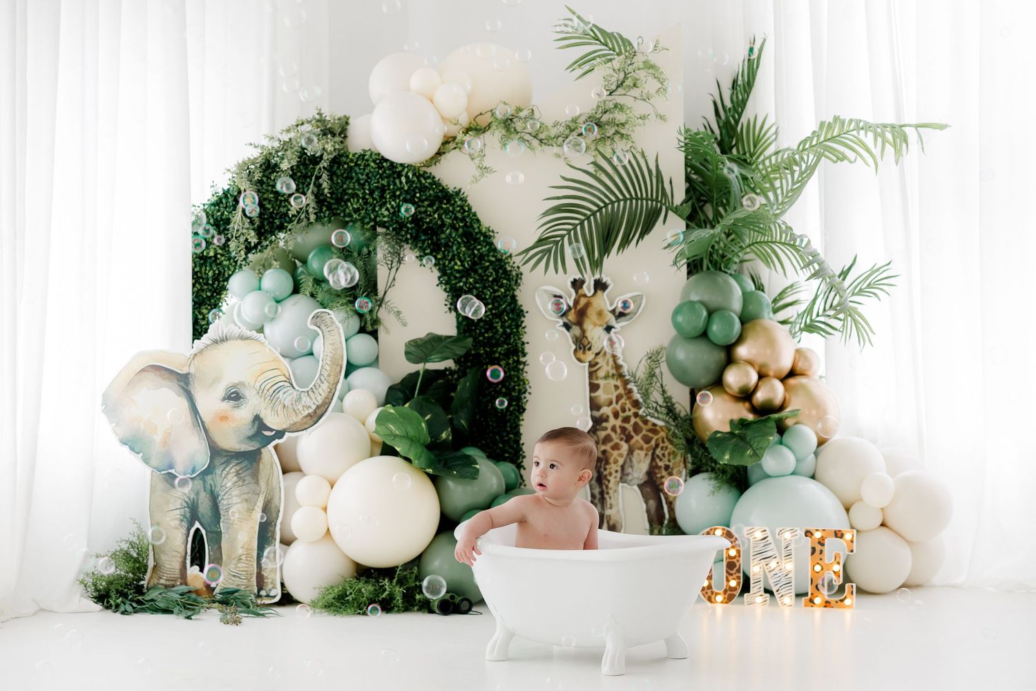 Elegant white and green tropical baby shower decorations with palm leaves, balloons, and gold safari animal accents.