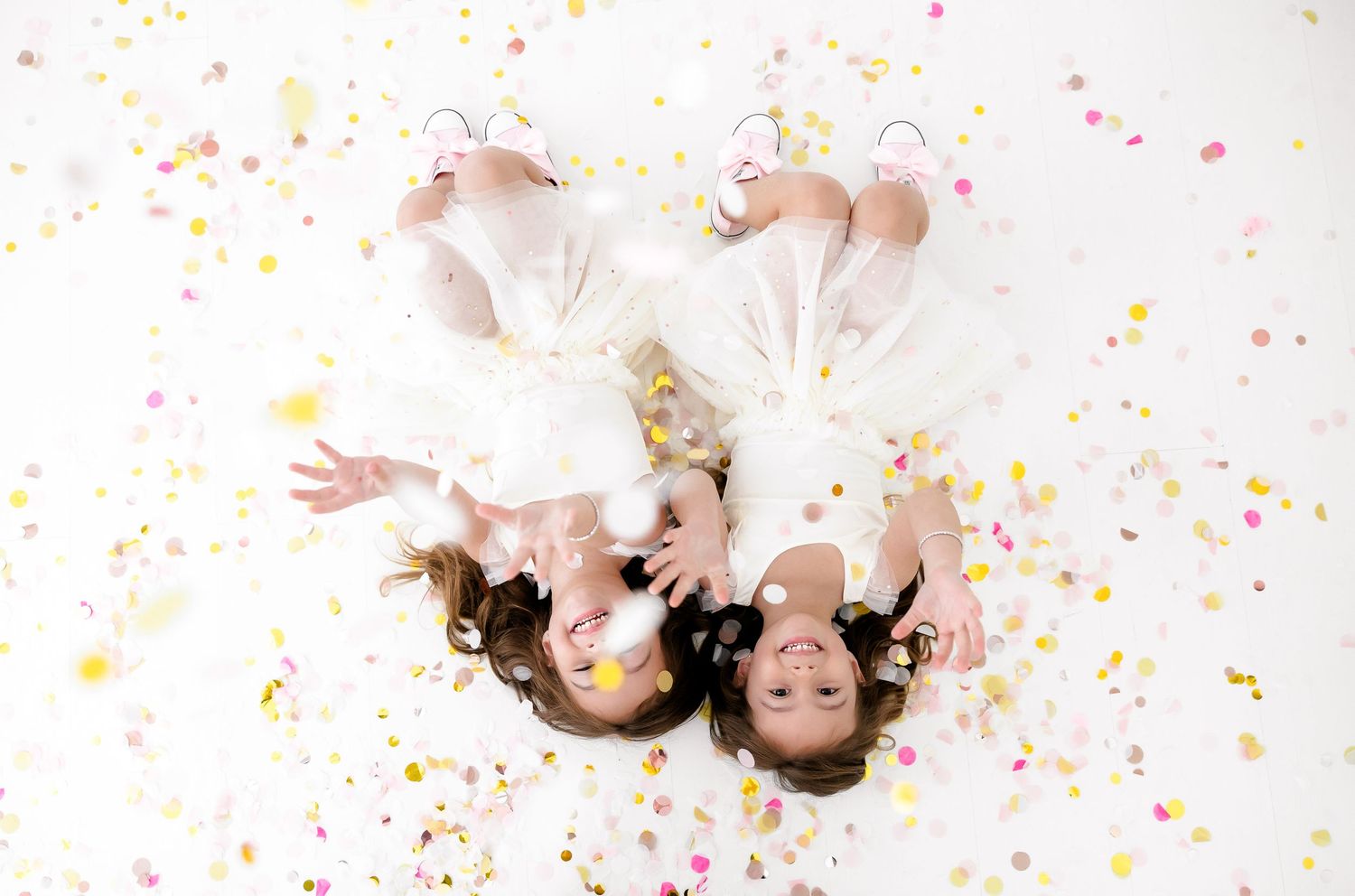 A person lying on white background with pink and yellow confetti scattered around them in a dreamy pose.