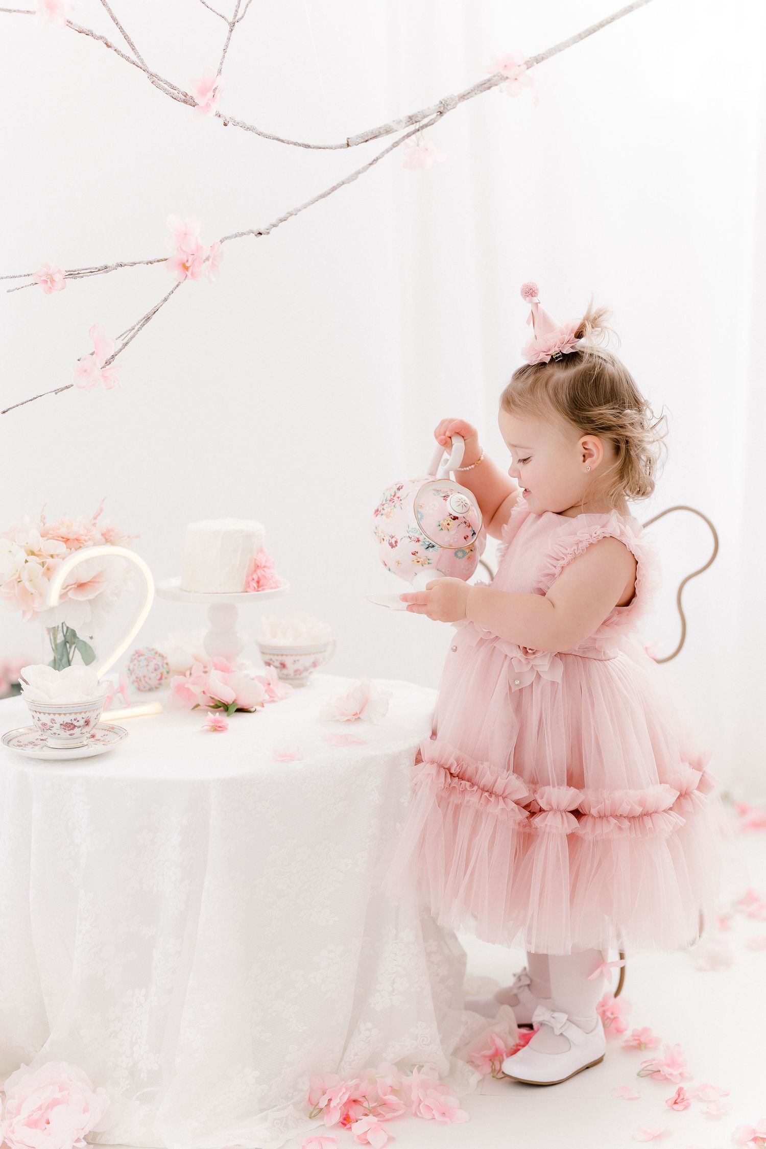 Little girl in pink tulle dress plays at elegant tea party setting with cherry blossoms.