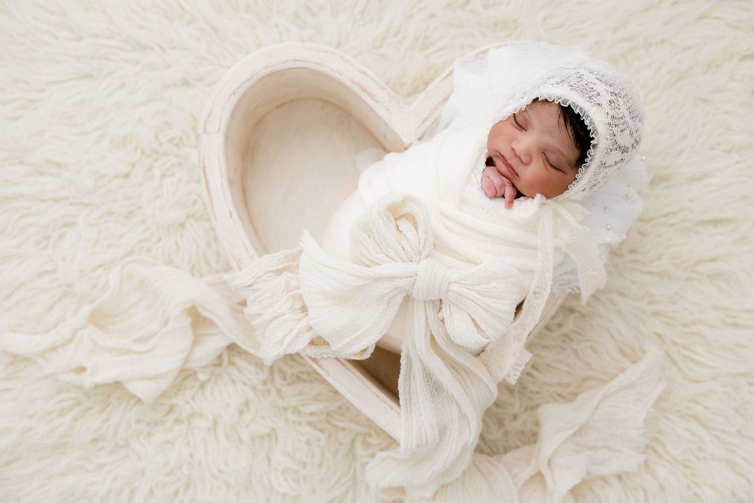 Angelic newborn photography on cream textured backdrop with flowing white fabric.