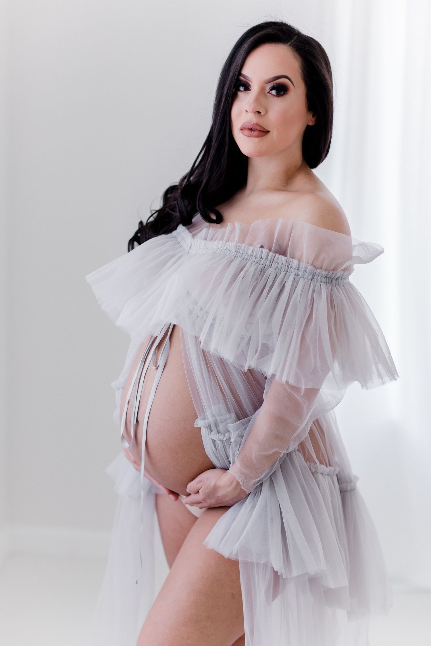 Dreamy maternity photoshoot with delicate ruffled tulle overlay in an all-white studio.