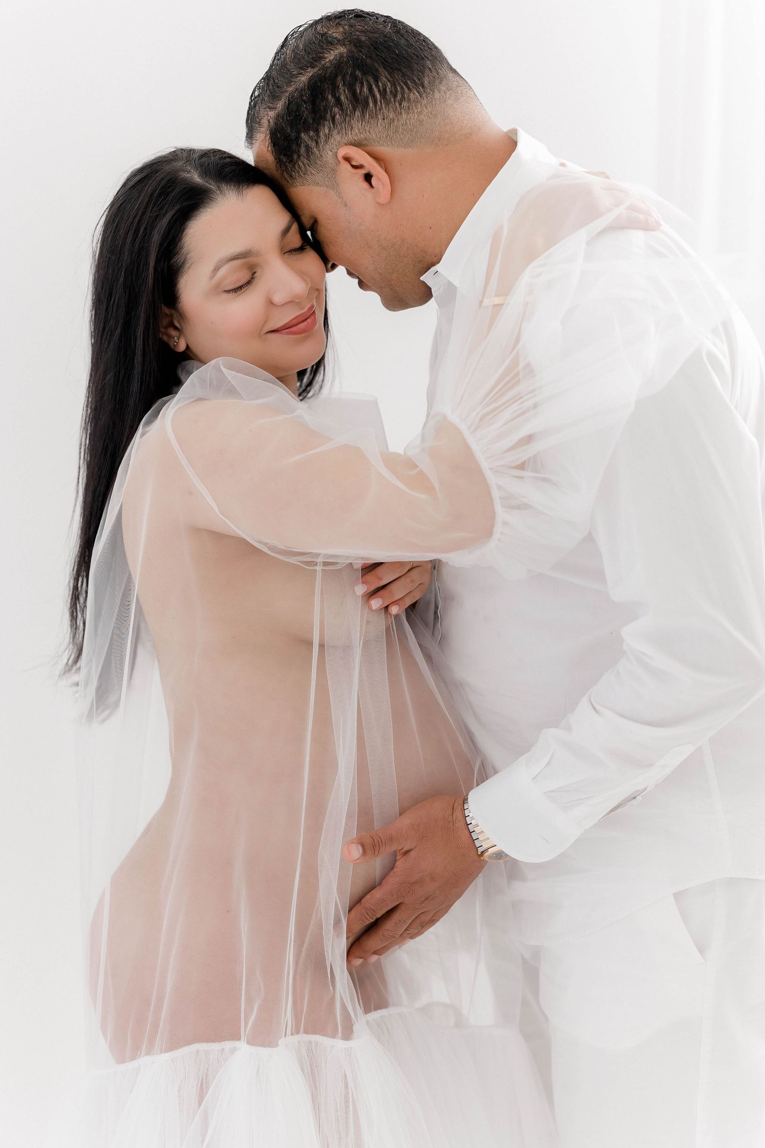 Intimate couples maternity photography session in white sheer fabrics.
