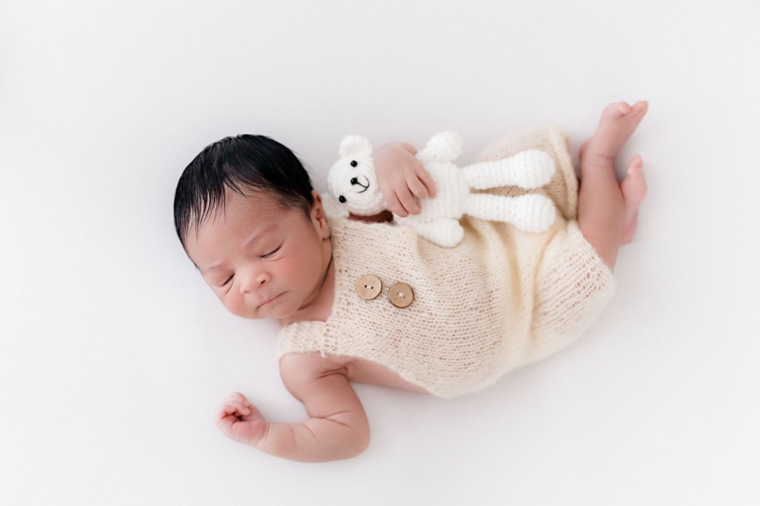 Sleeping newborn baby in cream colored outfit lying on white background.