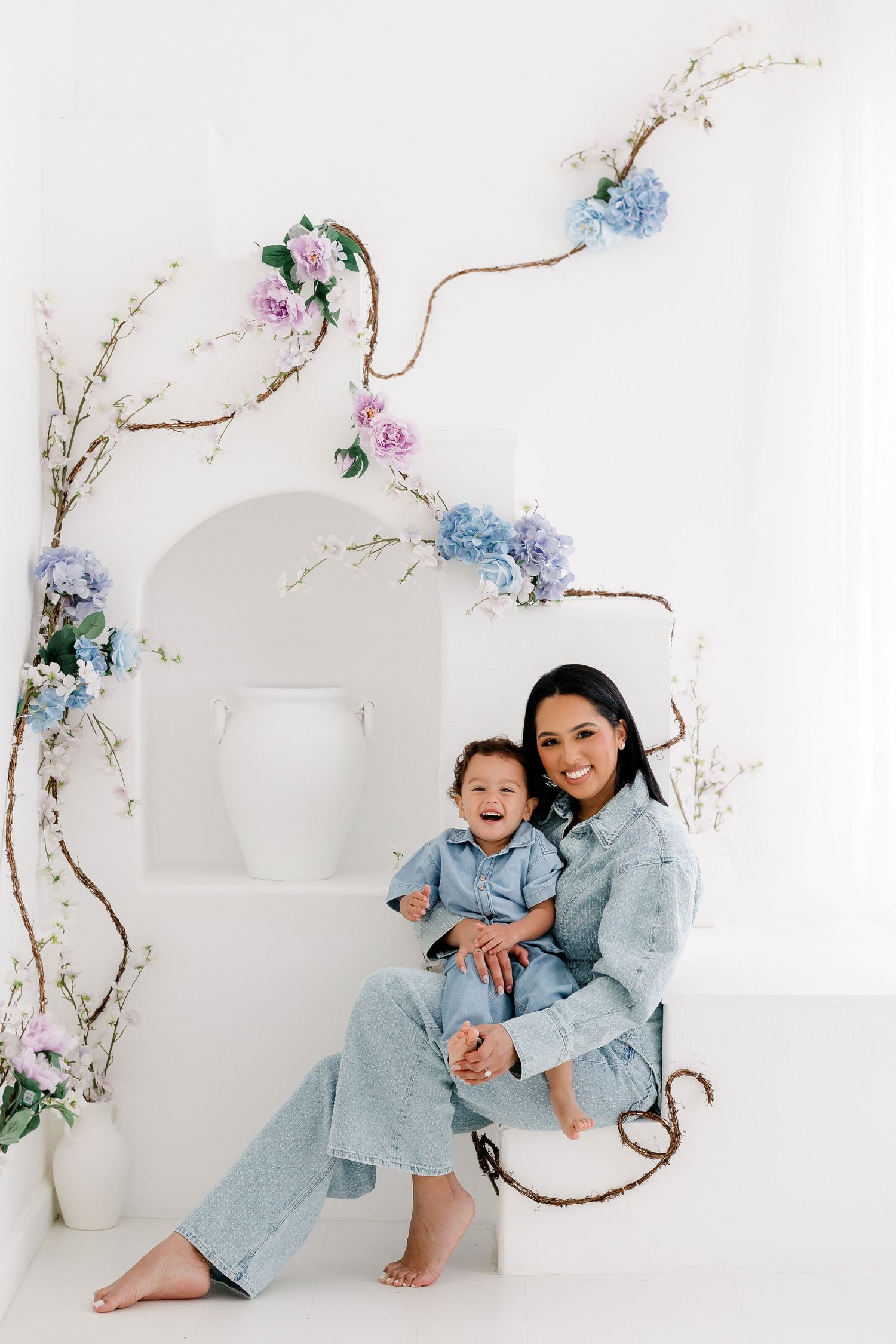 Two people in matching light blue outfits pose playfully against a white backdrop with delicate floral branches.