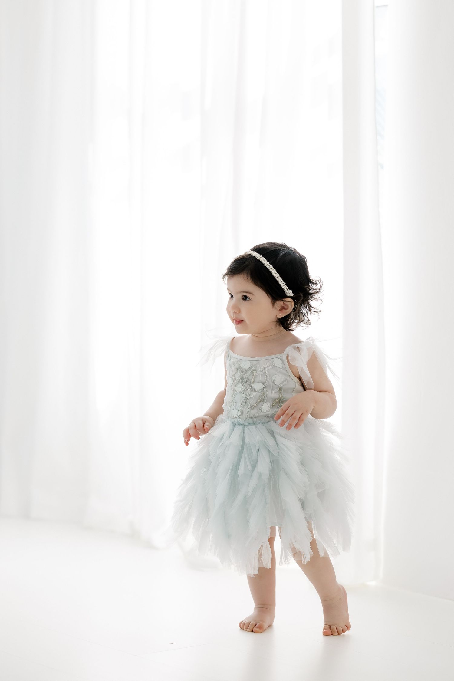 A toddler in a light blue tulle dress twirls and dances against a white backdrop in a series of playful poses.