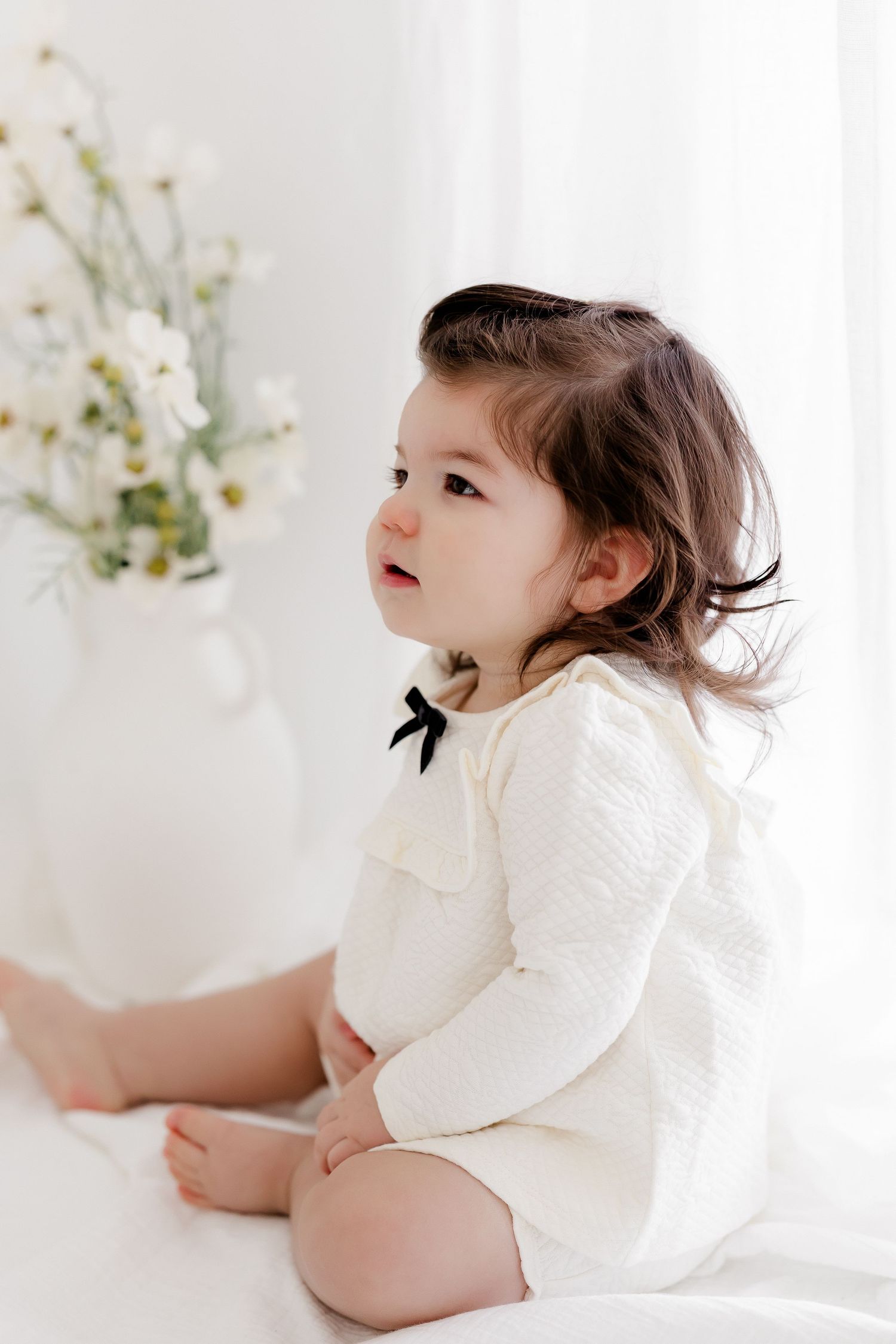 A child in a white dress sits on a white backdrop in a series of ethereal studio portraits.