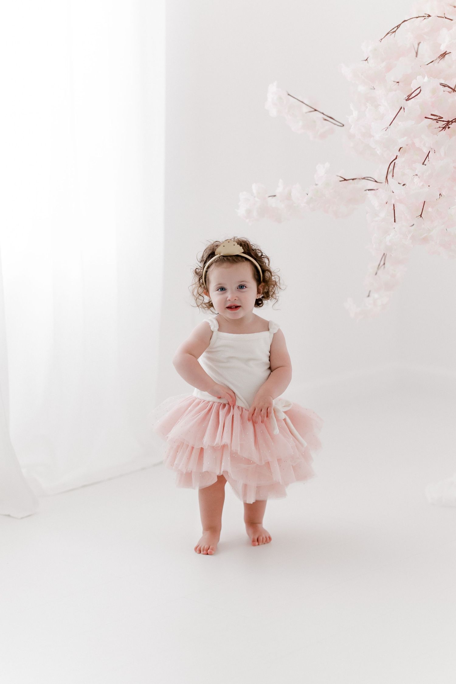 Sweet photoshoot with pink tulle dress against soft white background and cherry blossoms.