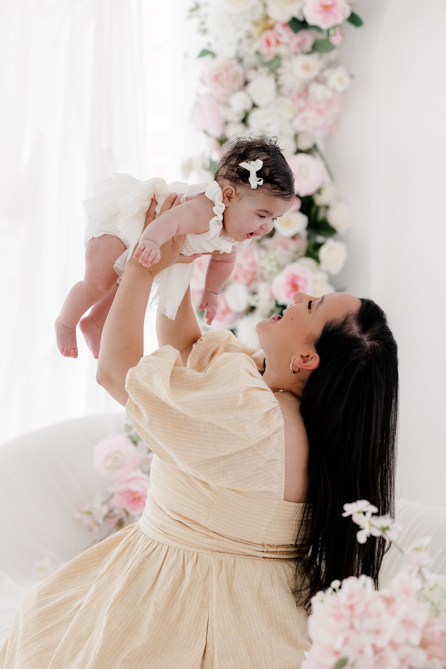 A tender moment between parent and baby surrounded by soft pink and white floral decorations in a bright setting.