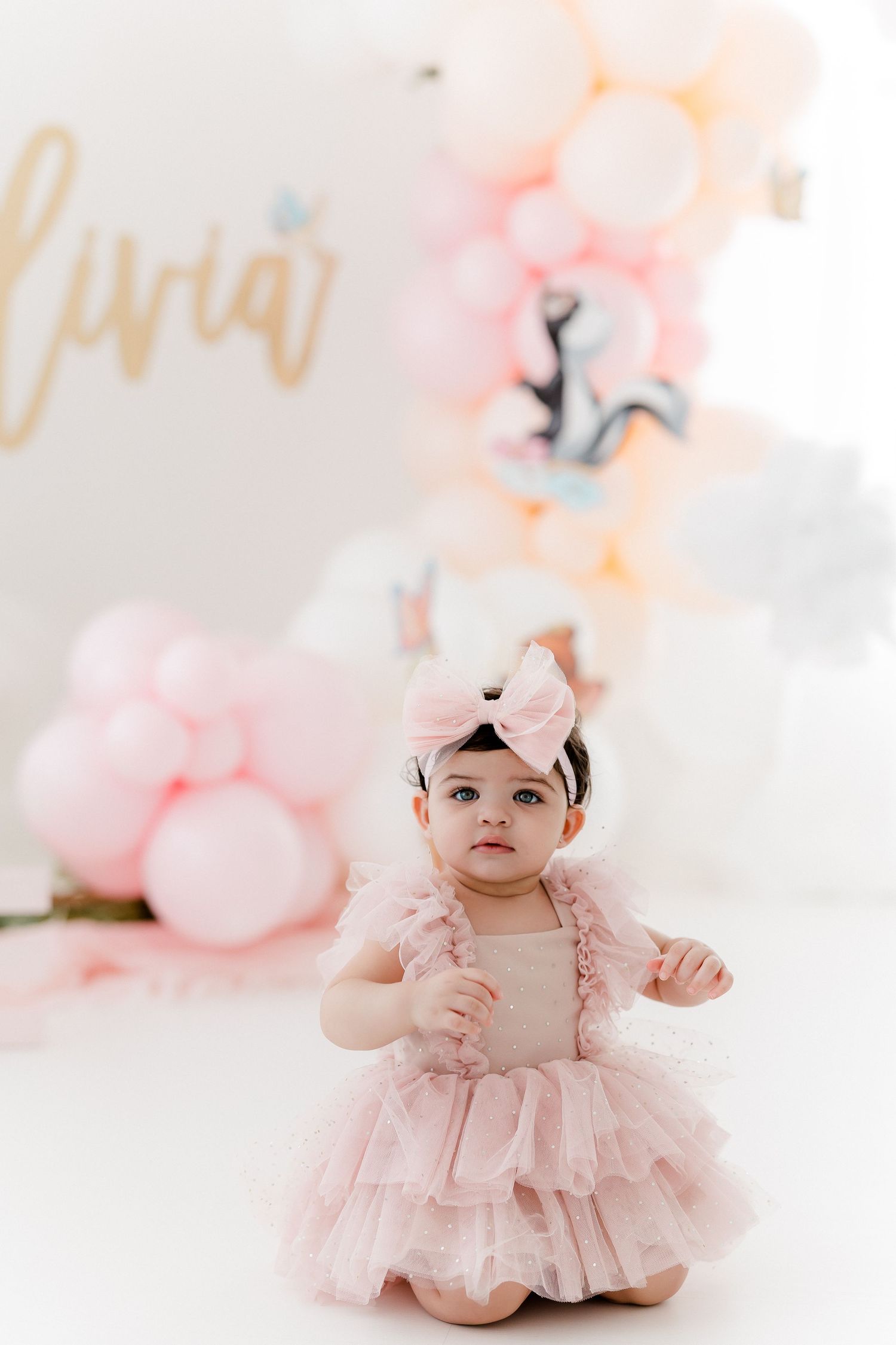 Delicate pink tulle dress against soft white backdrop with floral accents.
