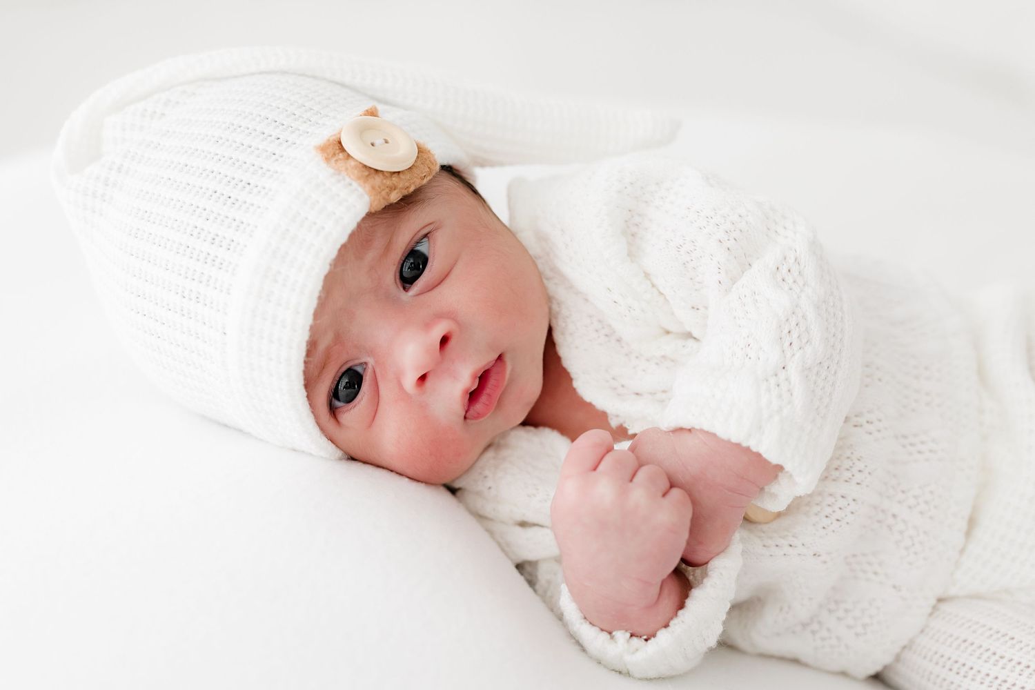 Newborn baby wrapped in soft white blanket lies peacefully against white background.