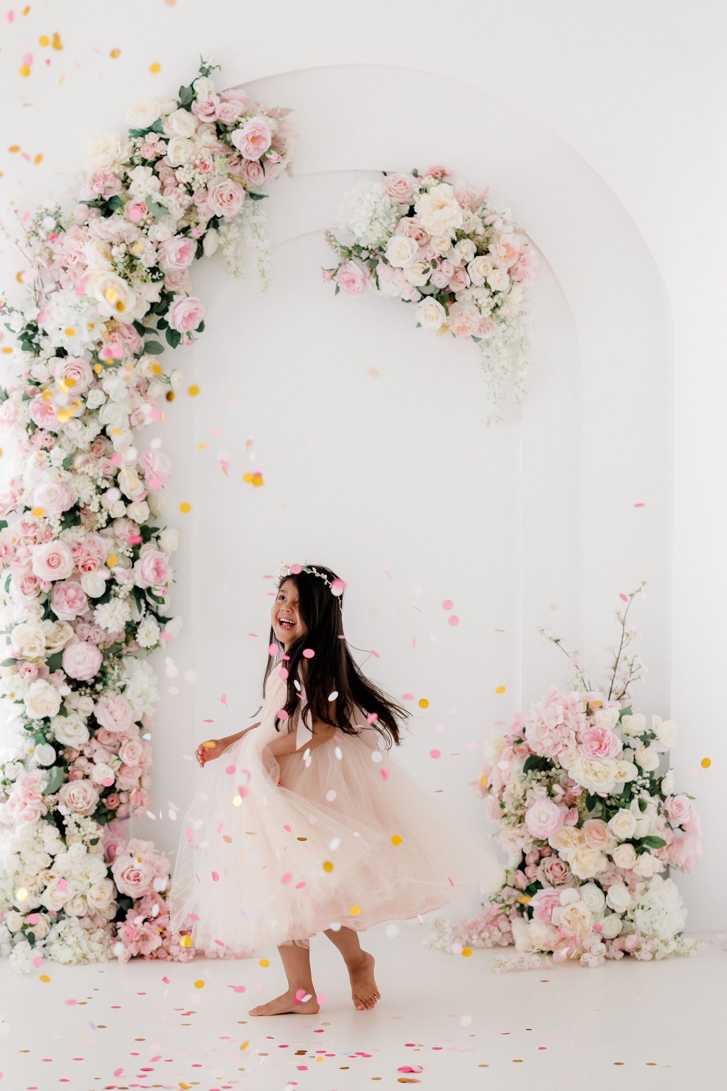 Dreamy floral photo session with pink and white roses decorating white backdrop as rose petals float through the air.