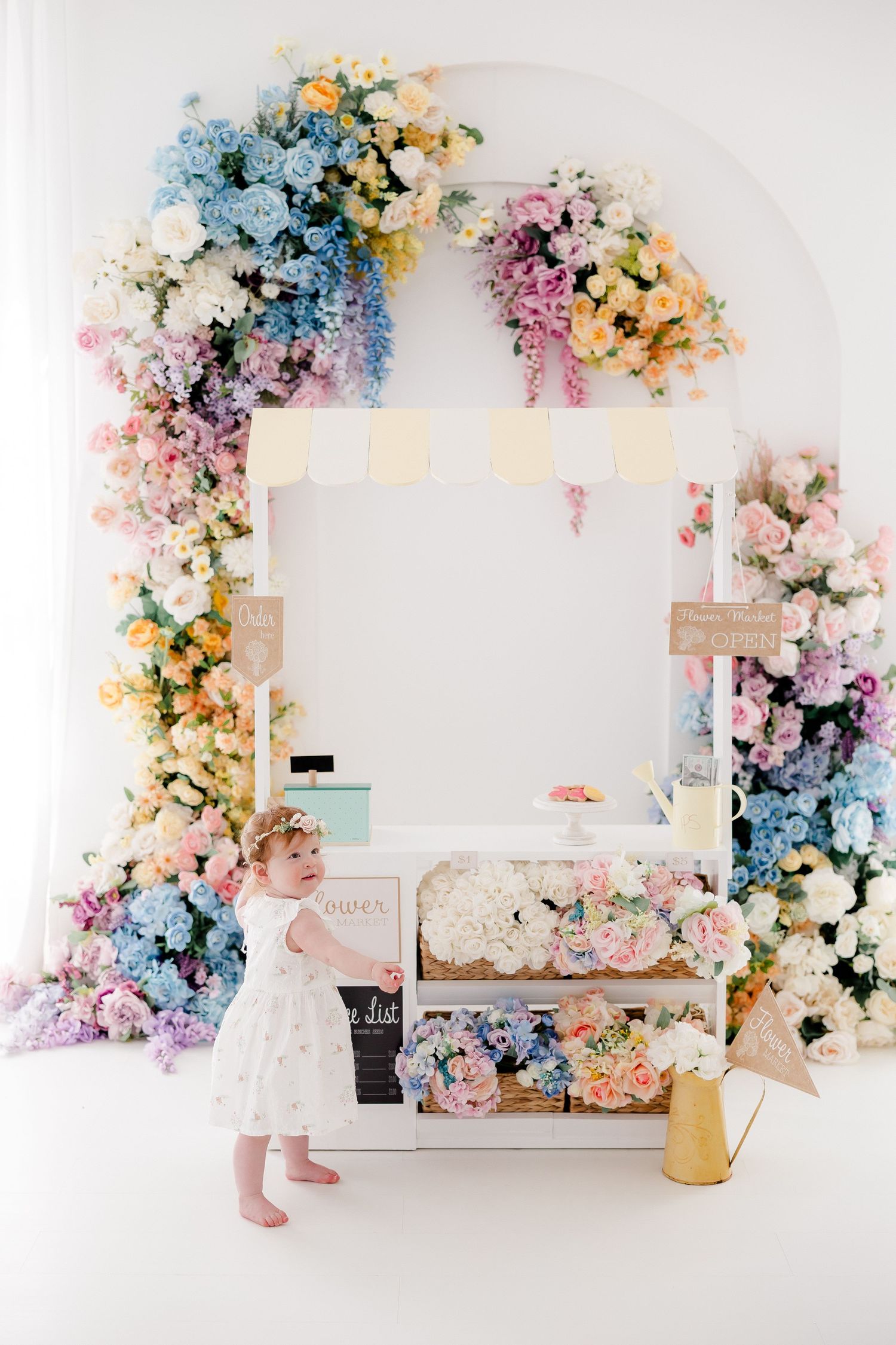 Beautiful floral backdrop with pink, blue and yellow flowers creates a dreamy setting for a cake smash photography session.