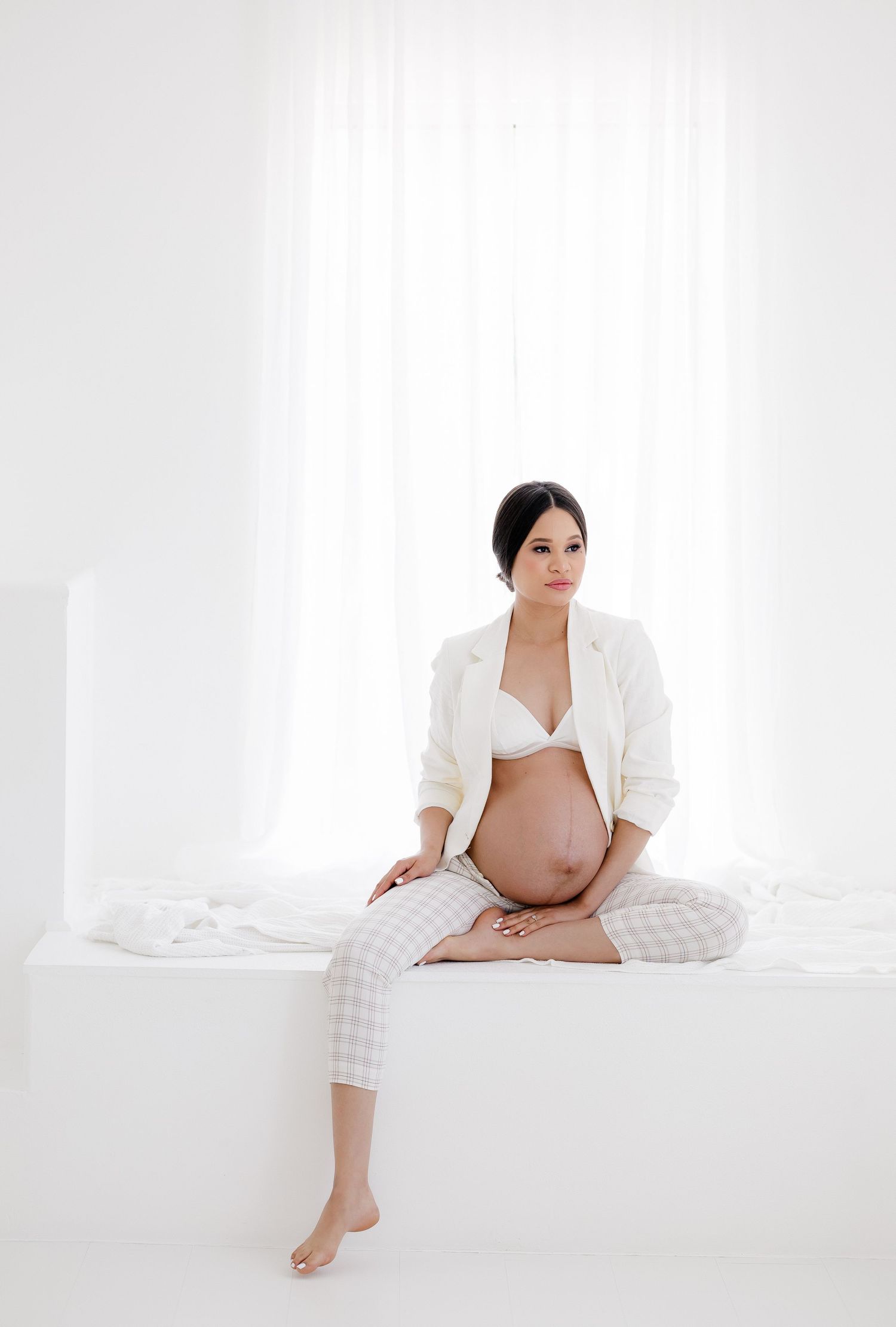 Minimalist maternity photos in white against bright background showing expectant mother in casual pose.