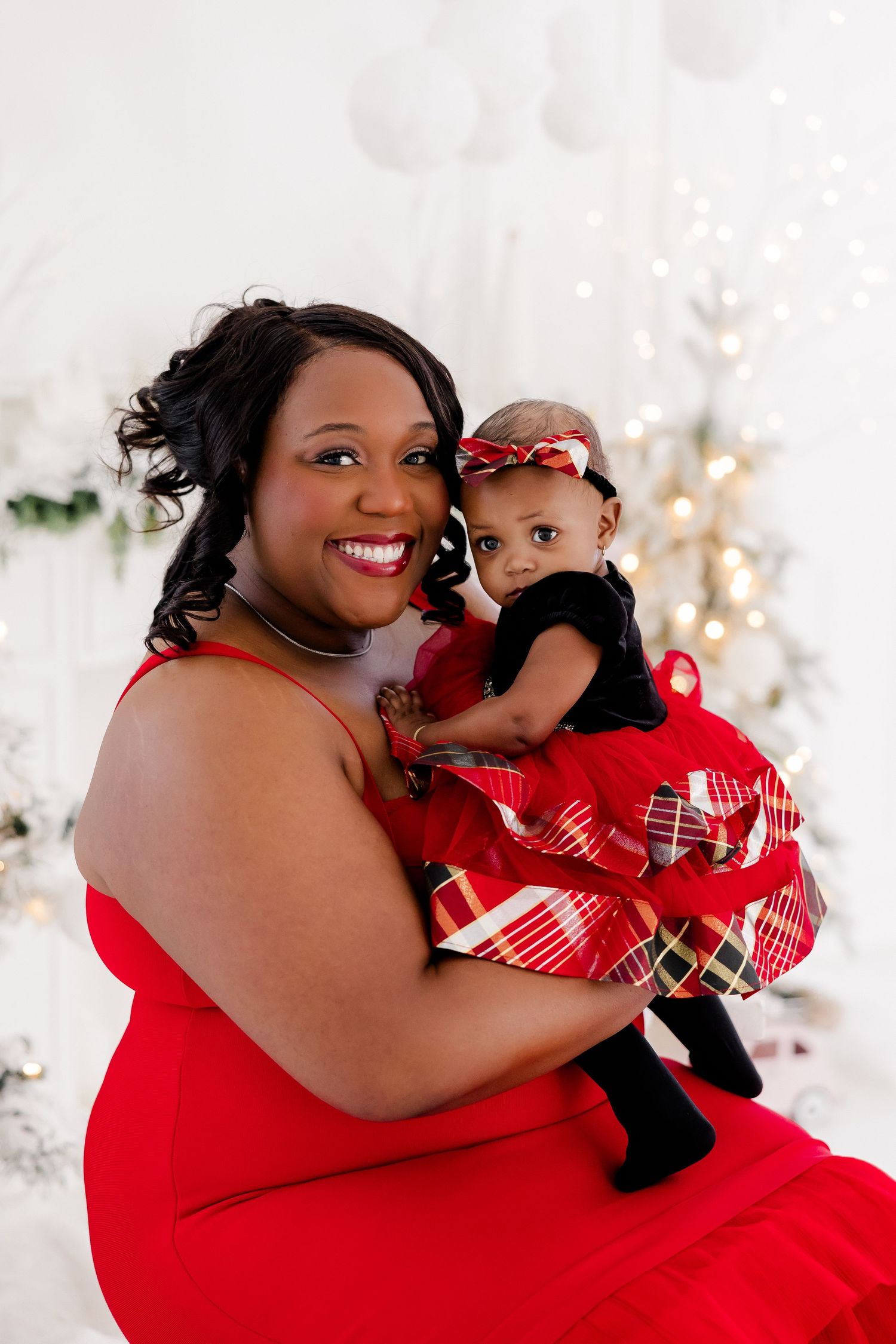 Festive holiday portrait in red dresses against white Christmas backdrop.