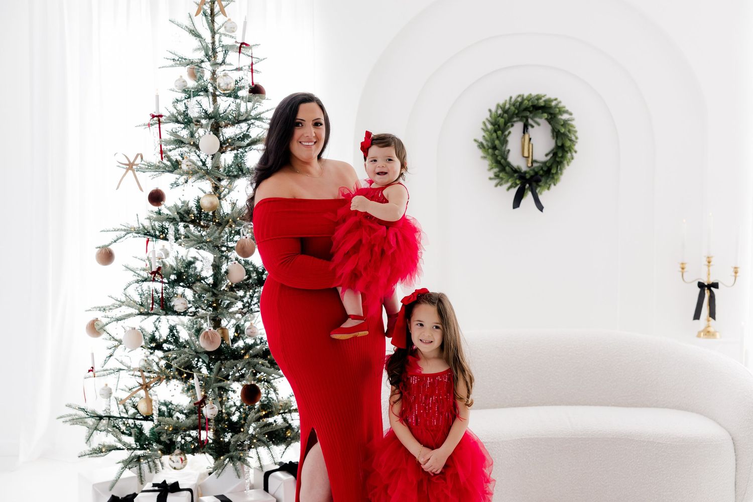 Family holiday photoshoot with red outfits against a white backdrop with Christmas decorations.