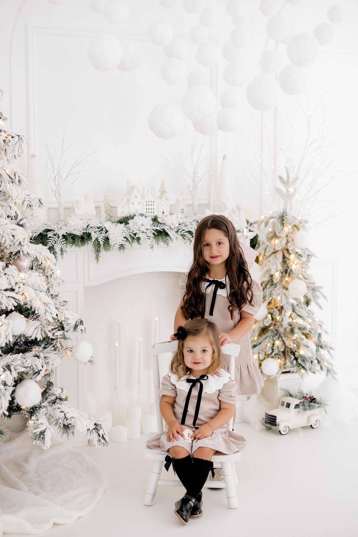 Two children pose with a teddy bear in a winter wonderland studio setting with flocked Christmas trees.