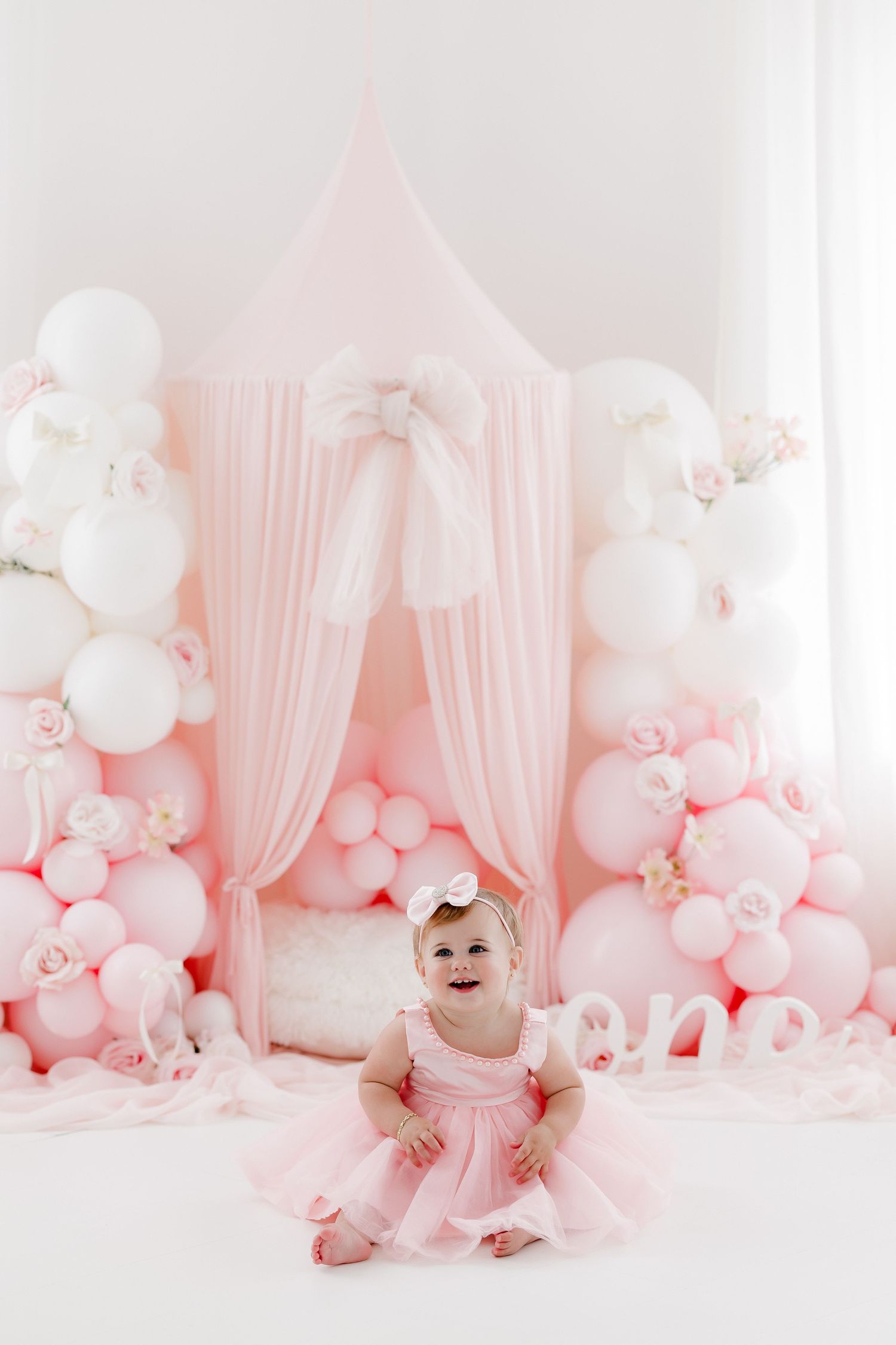 Pink princess-themed setup with tulle canopy and balloon arch for baby photoshoot.