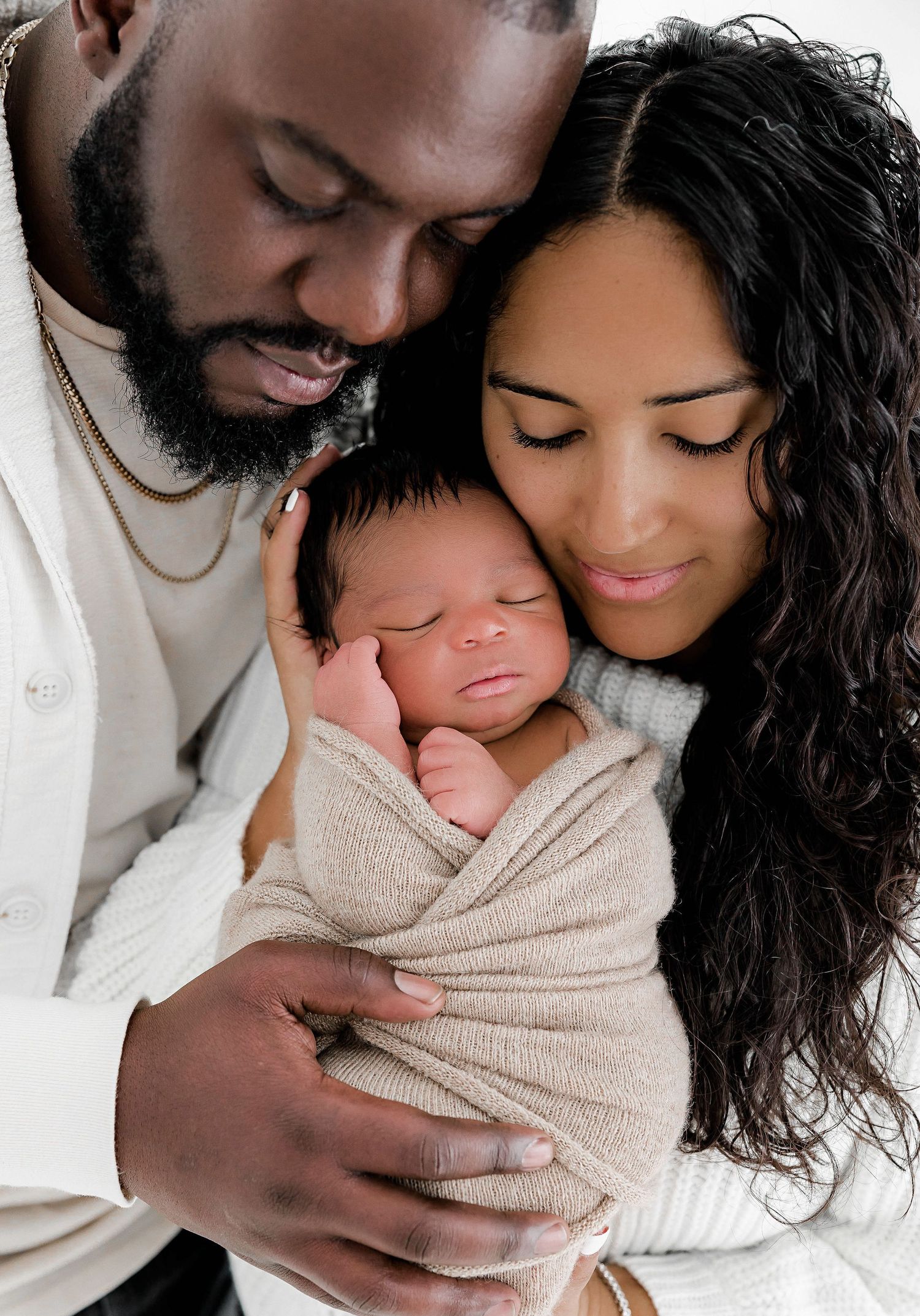Family shares intimate moment with newborn wrapped in beige swaddle.