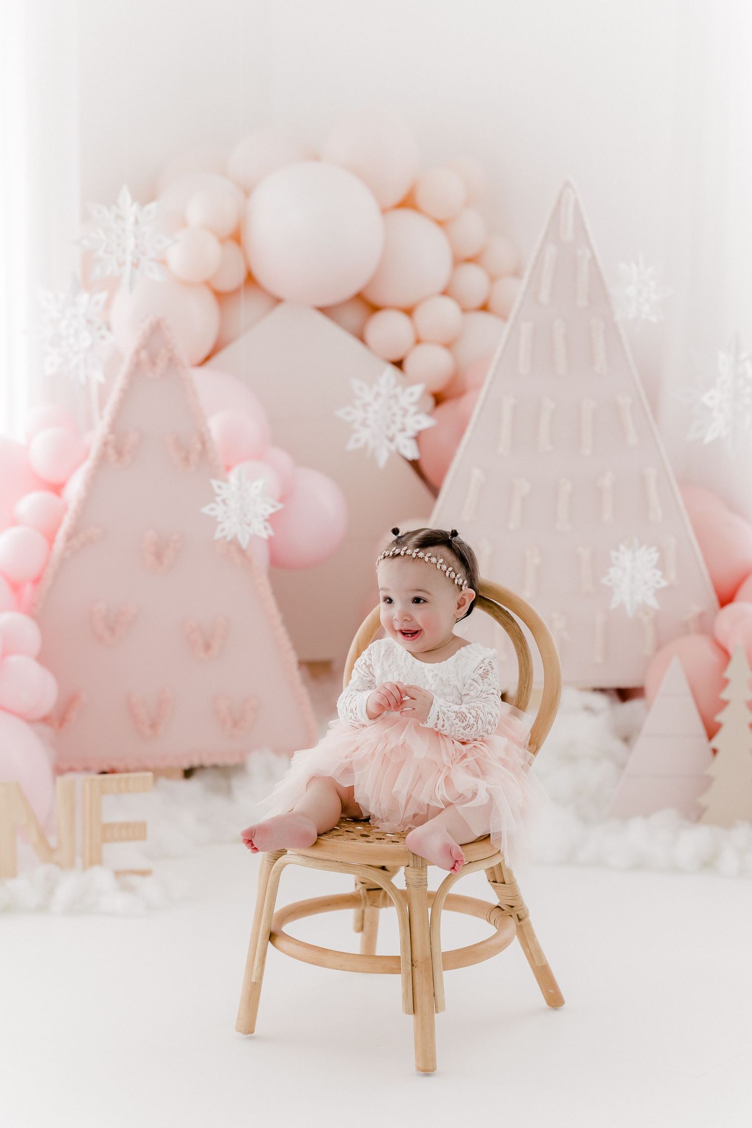 Dreamy pink and white winter wonderland setup with balloon arch and wooden chair.