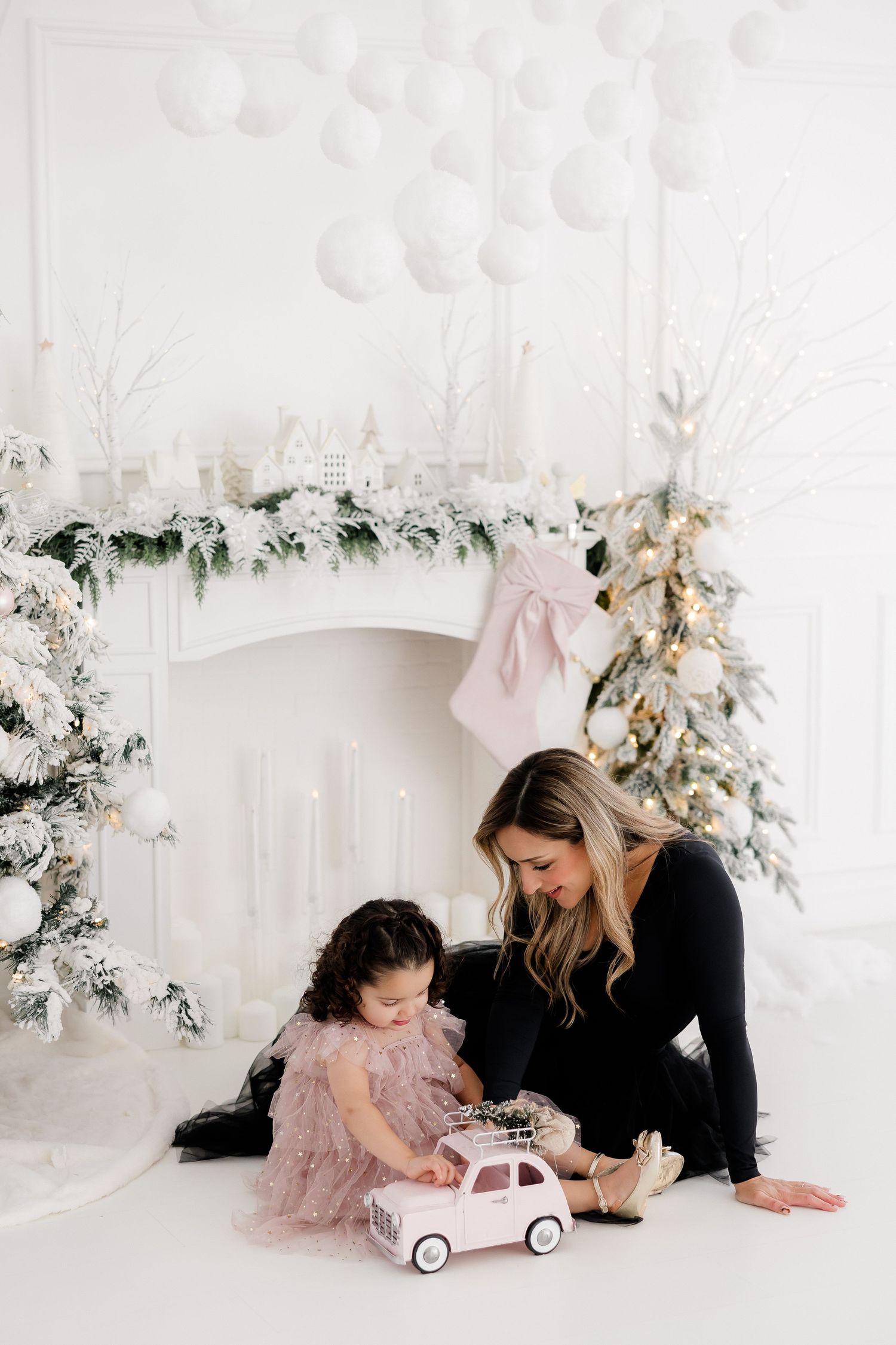 Parent and child playing with toy car in elegant white Christmas setting with flocked tree.