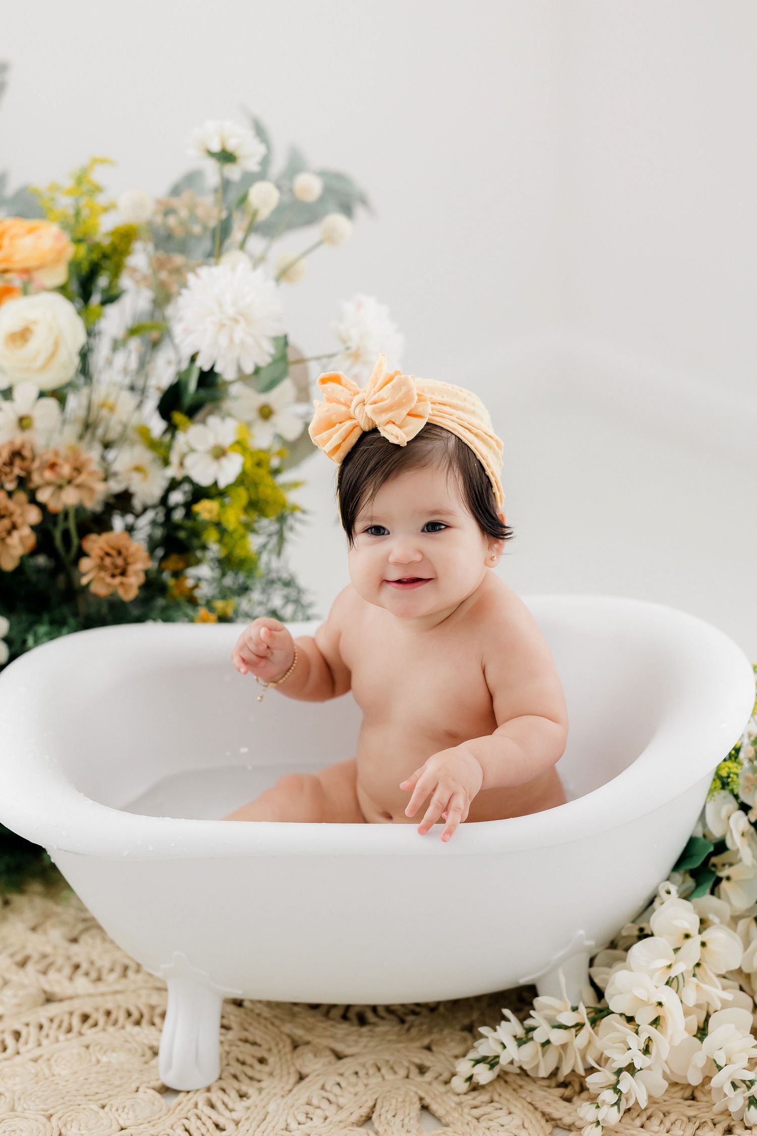 Sweet baby milestone photos in white bathtub surrounded by delicate spring flowers and greenery.