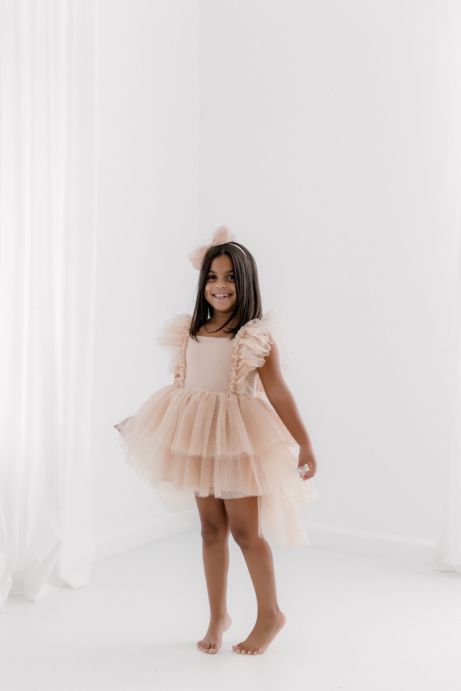 Young dancer in ruffled peach tulle dress smiles in bright studio setting.