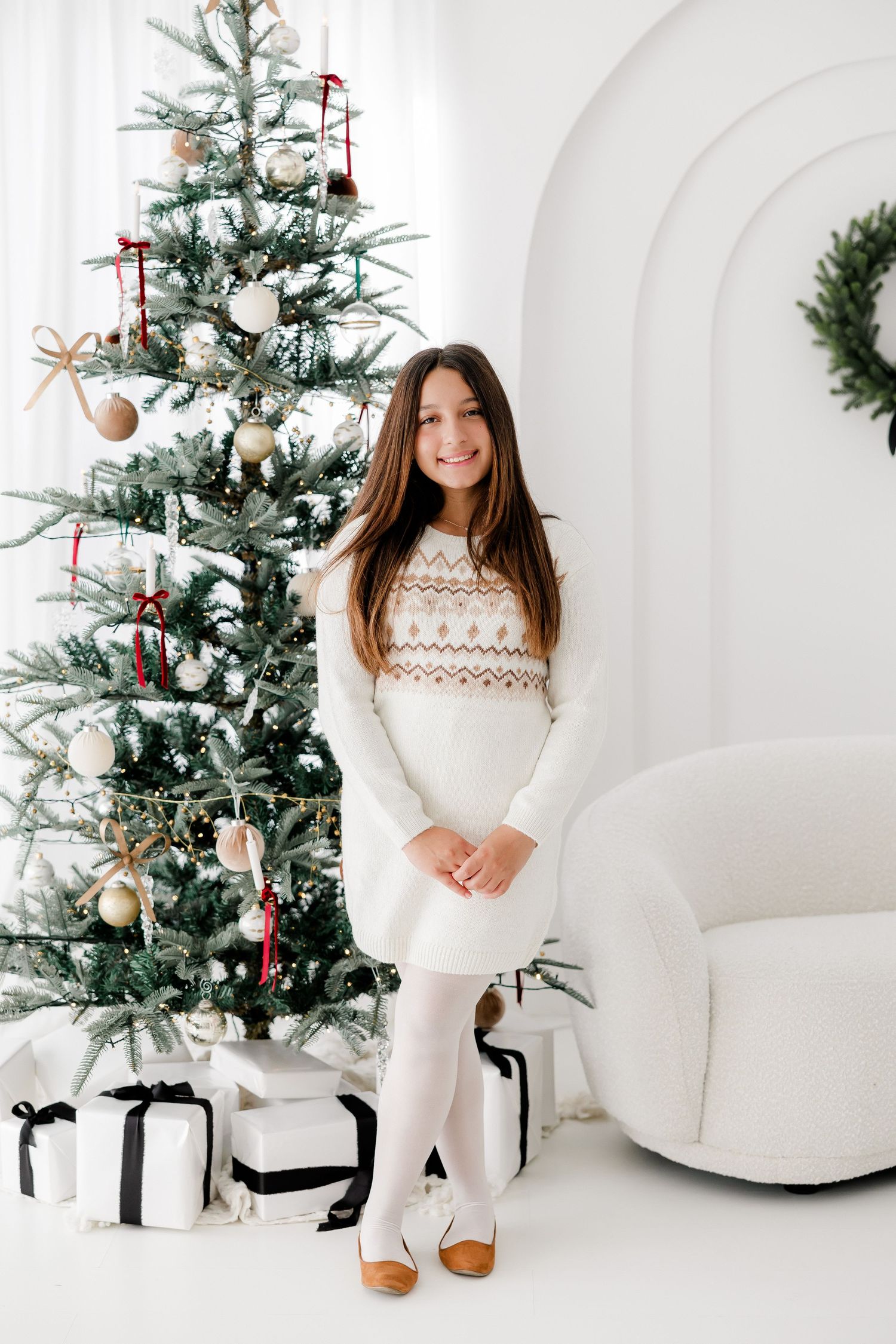 Winter portrait session with cozy white sweater against decorated Christmas tree backdrop.