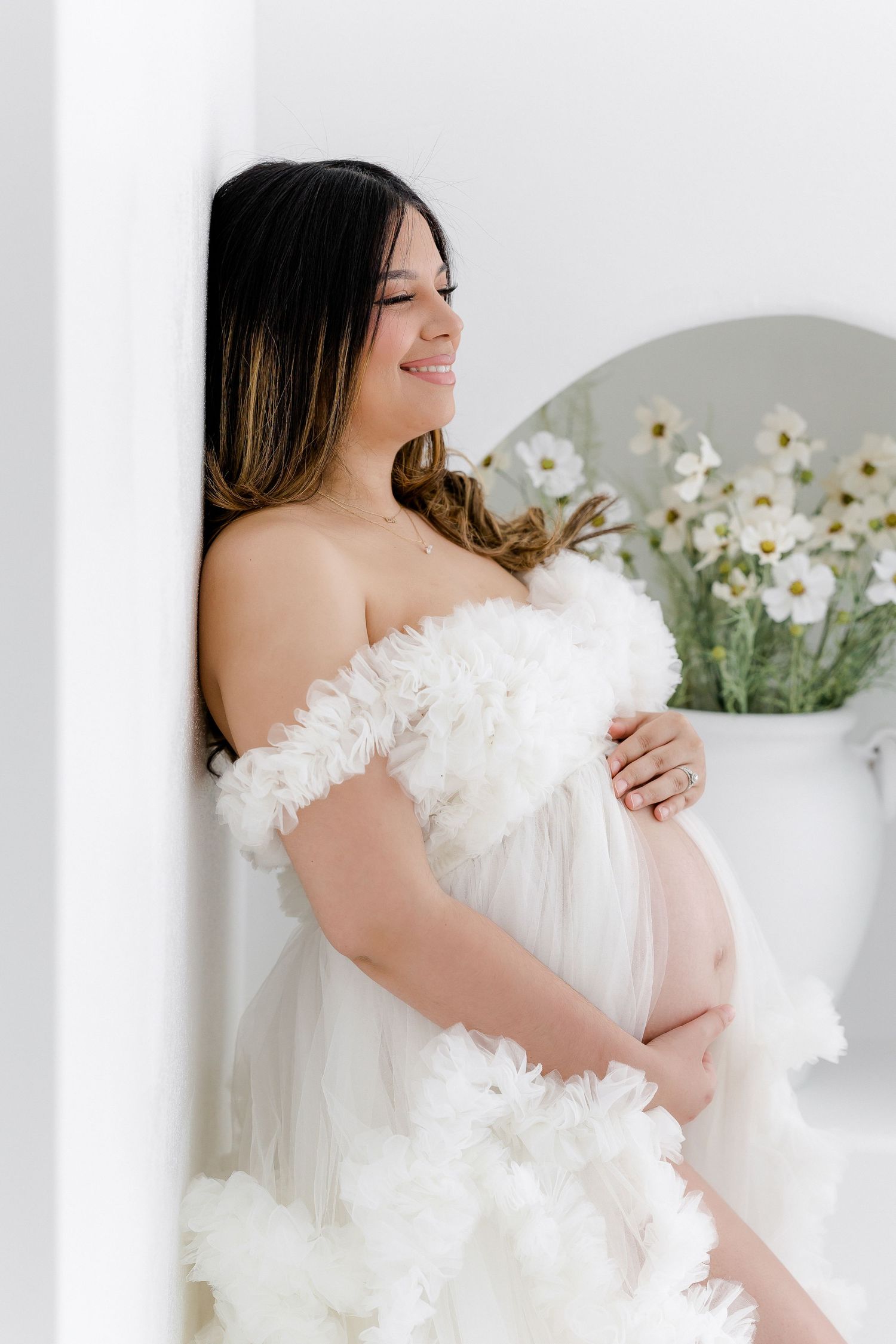 Elegant maternity photoshoot featuring white off-shoulder gown and spring flowers.
