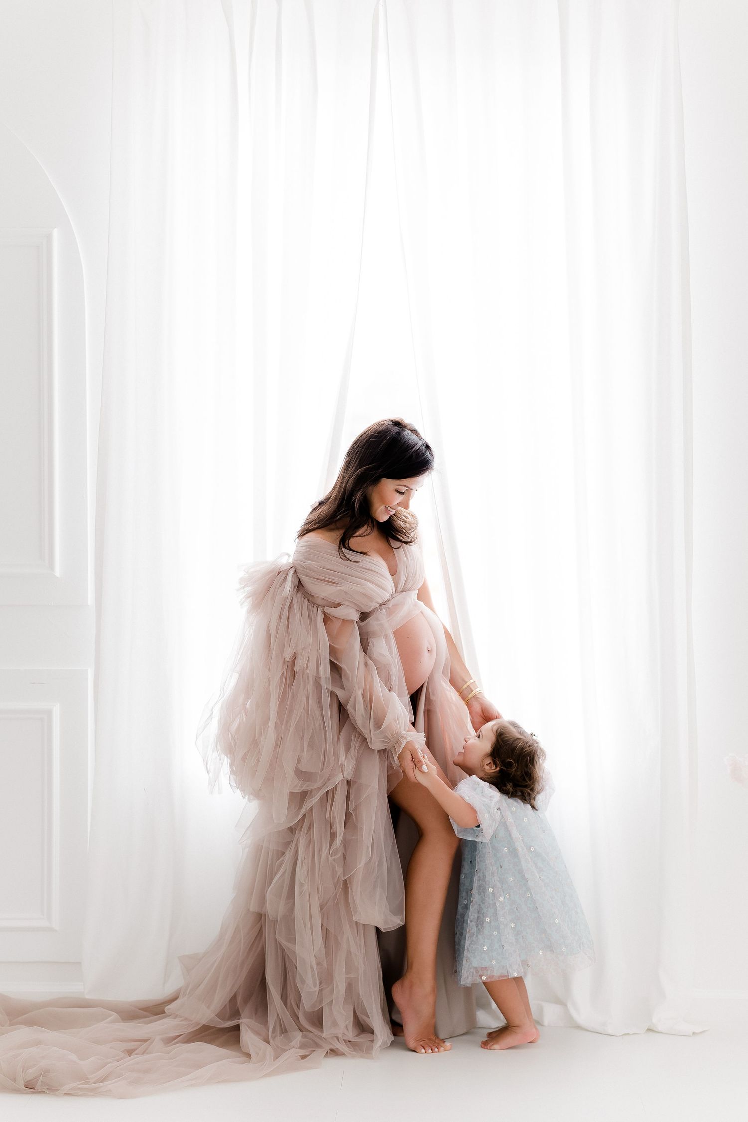 Ethereal studio portrait setup with flowing blush tulle dress against white backdrop.