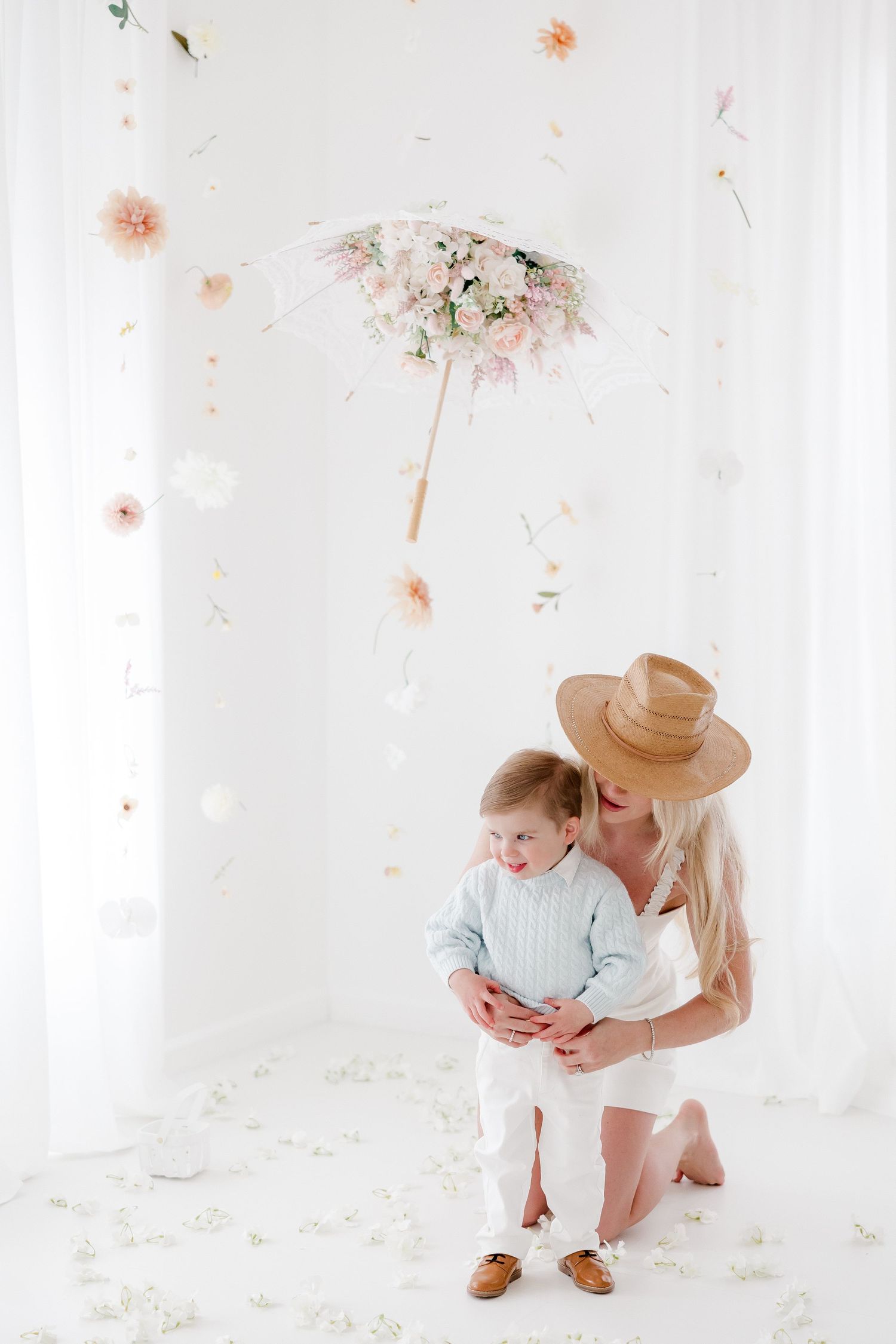Parent and child share tender moments in a bright white studio with delicate floral accents and soft natural lighting.