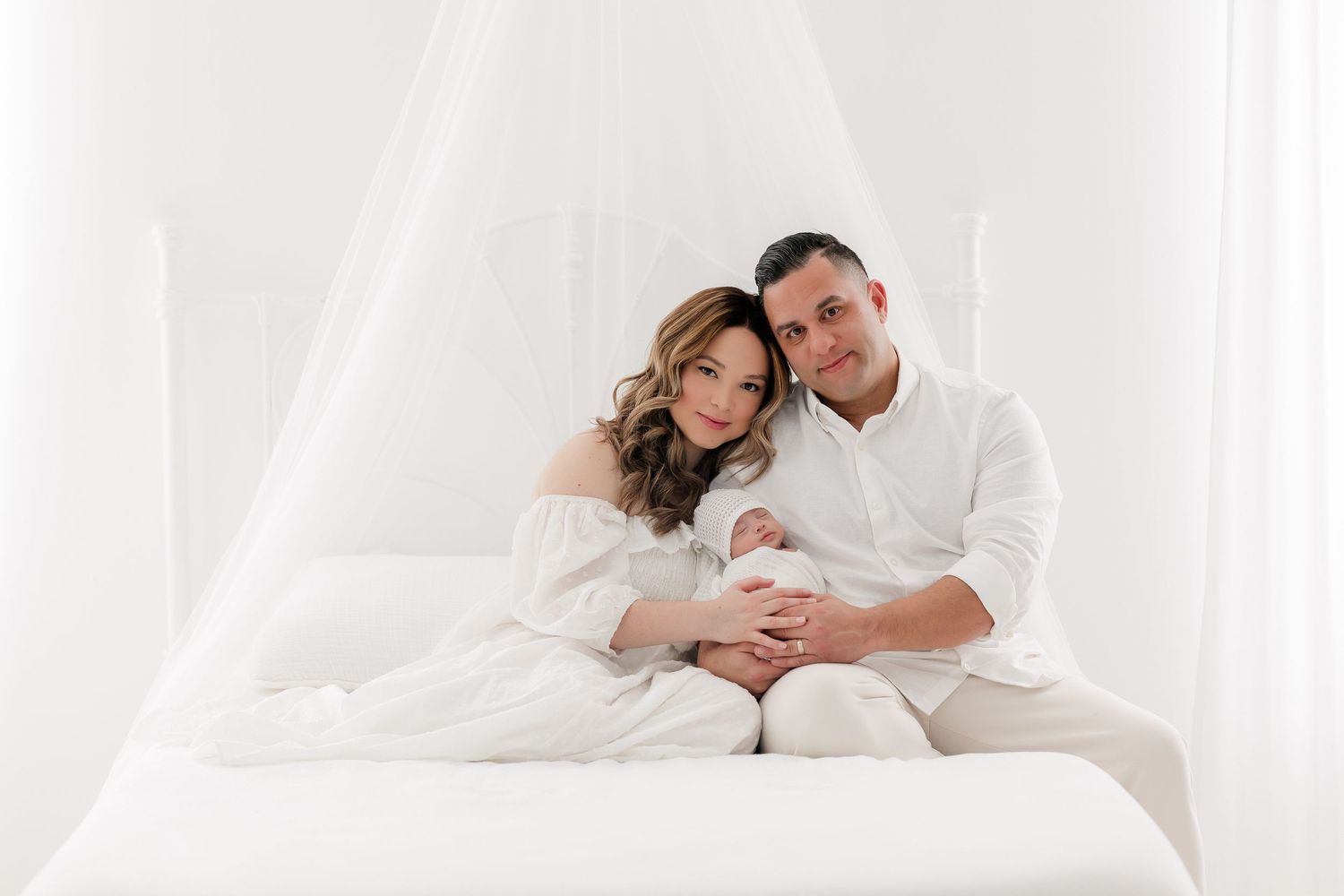 Intimate couple portrait session on white bedding with soft natural lighting.