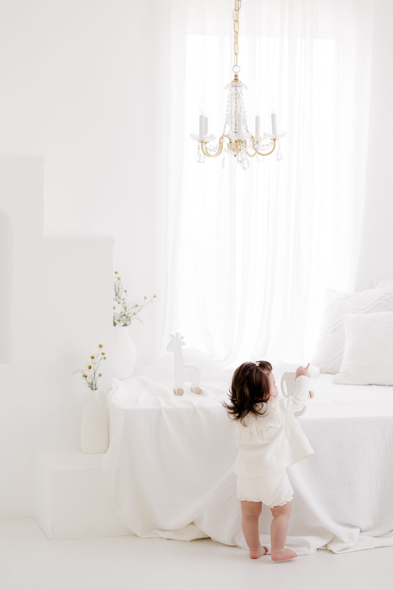 White chandelier hanging above draped fabric in minimalist setting.