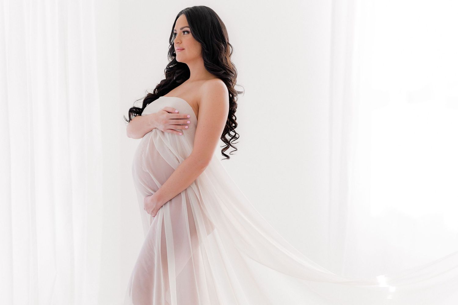Romantic maternity portraits with flowing fabric in bright white studio.