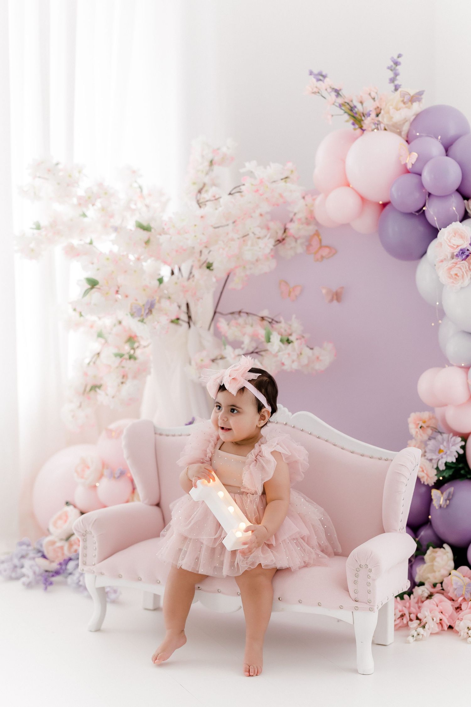 Baby photoshoot with pink and purple floral decorations and vintage white furniture.