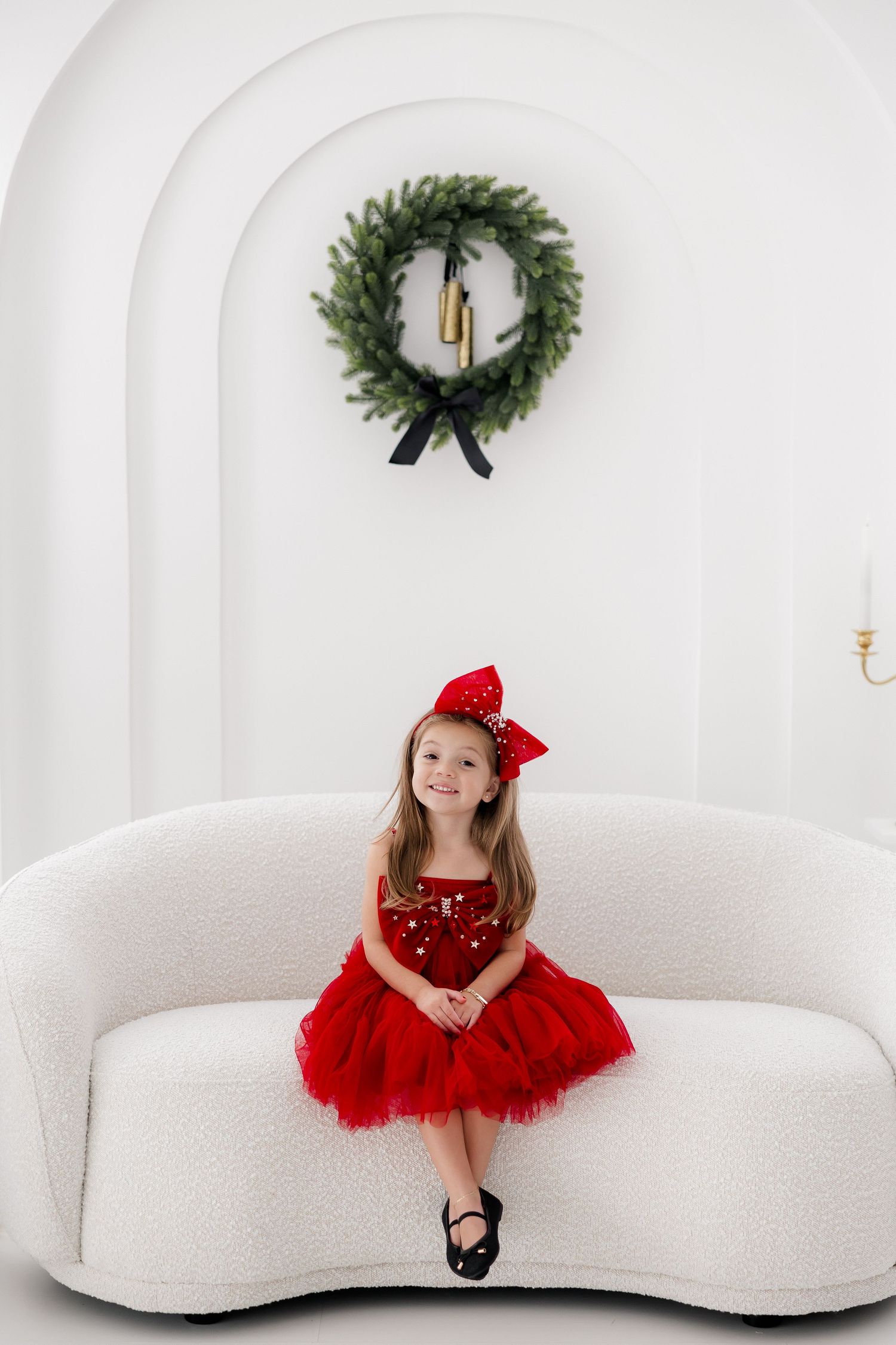 A festive red dress and bow create a striking contrast against a white studio backdrop with Christmas decor.