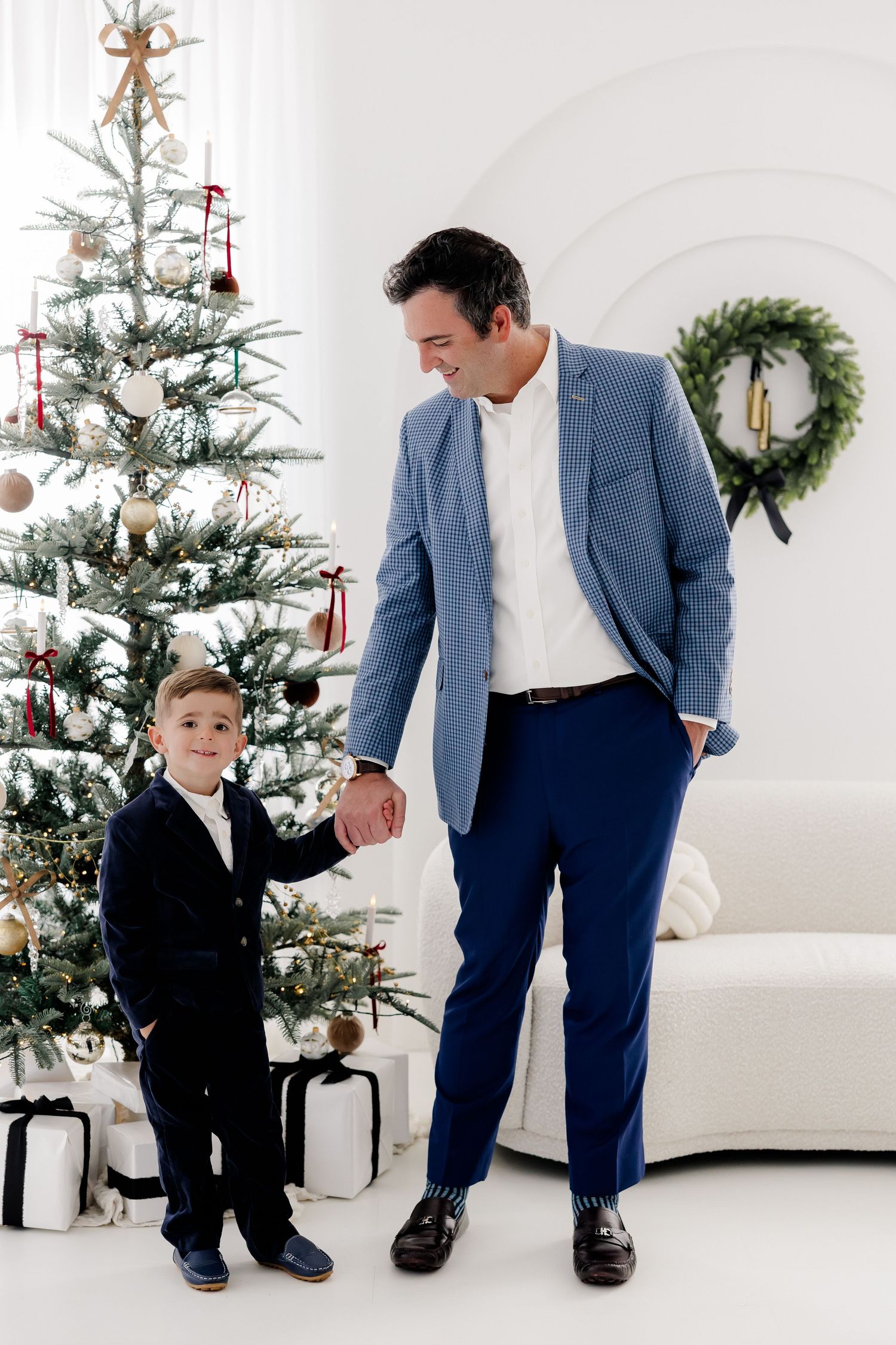 Stylish father-son moment captured in blue suit and formal wear against Christmas backdrop.