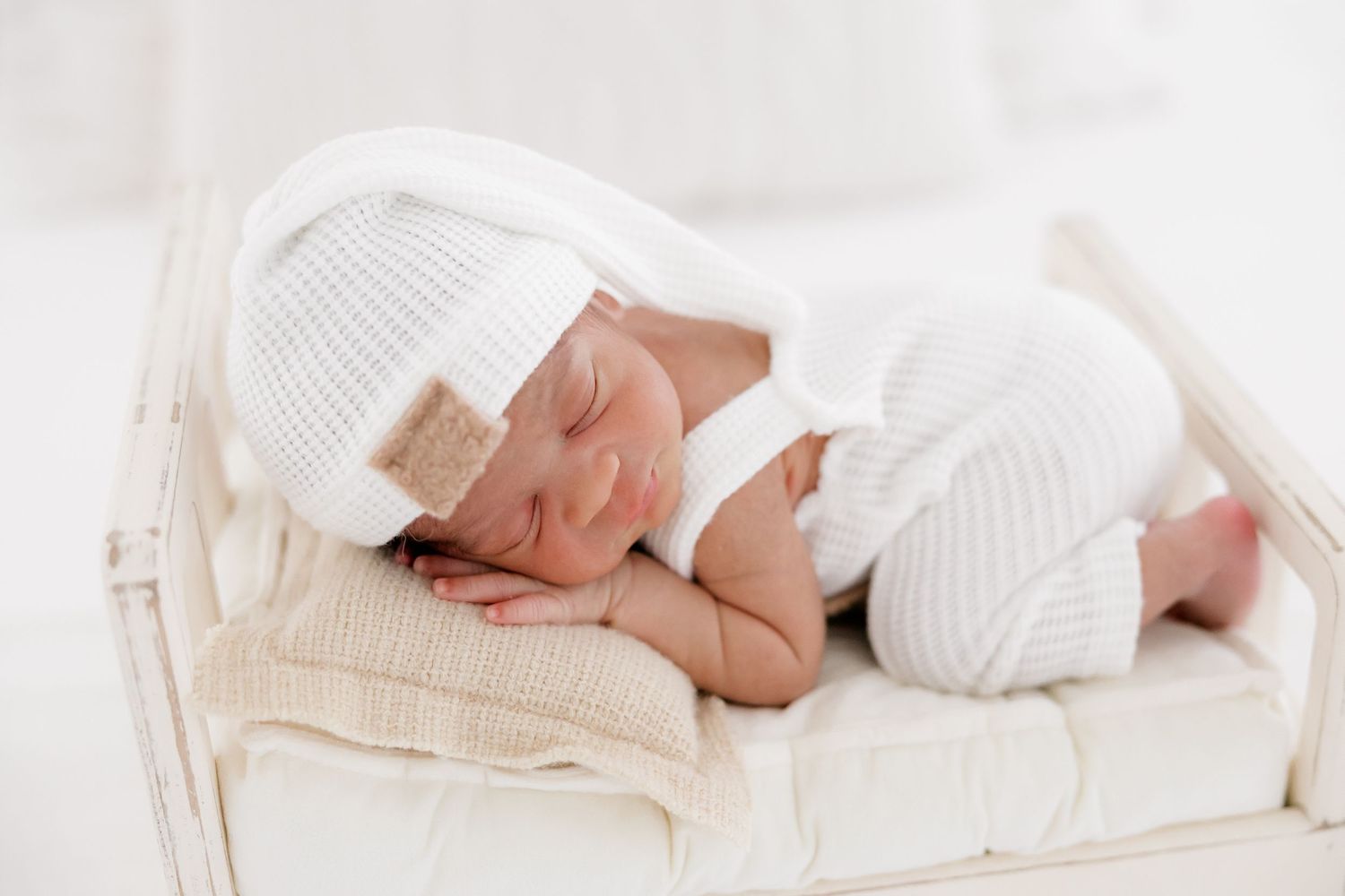 Newborn baby sleeping peacefully in soft white blankets and wraps during professional photography session.