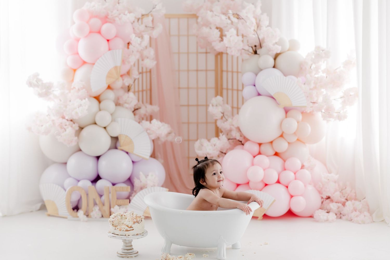 Luxurious bathtub setup with pink and white balloon arch decorations and elegant decor in soft pastel tones.