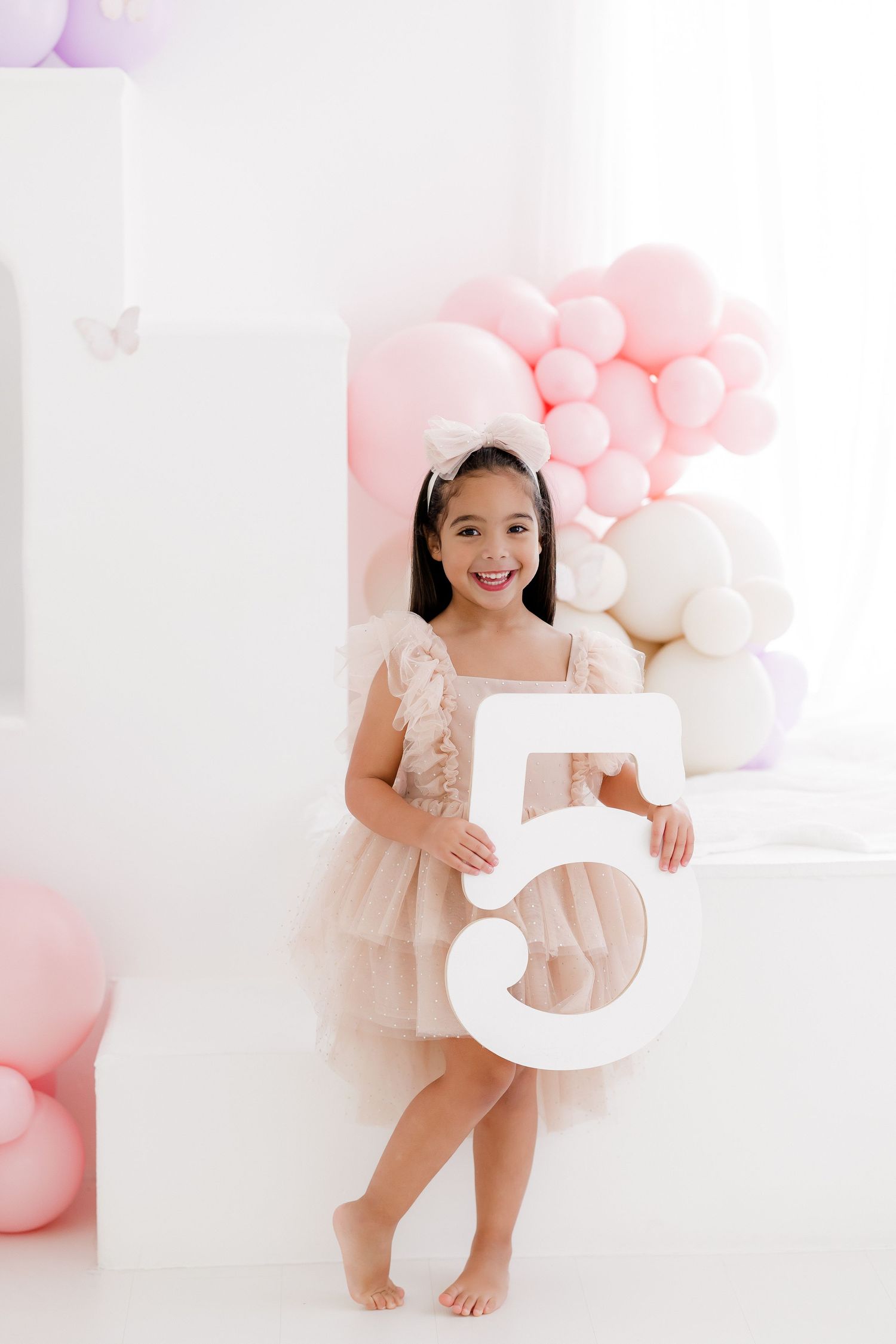 Sweet pink and white birthday photoshoot setup with balloons and decorative number props in a bright studio setting.